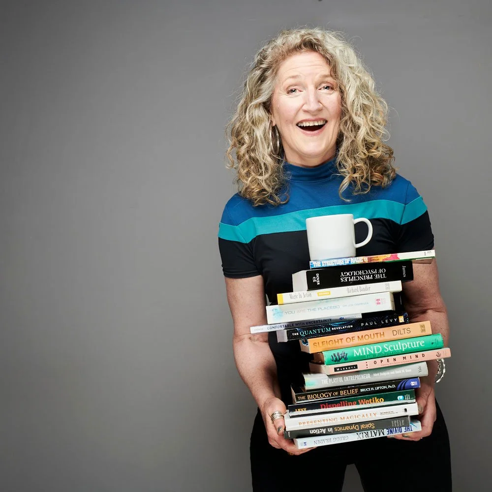 Woman laughing as she carries a tall stack of books with a white mug on top