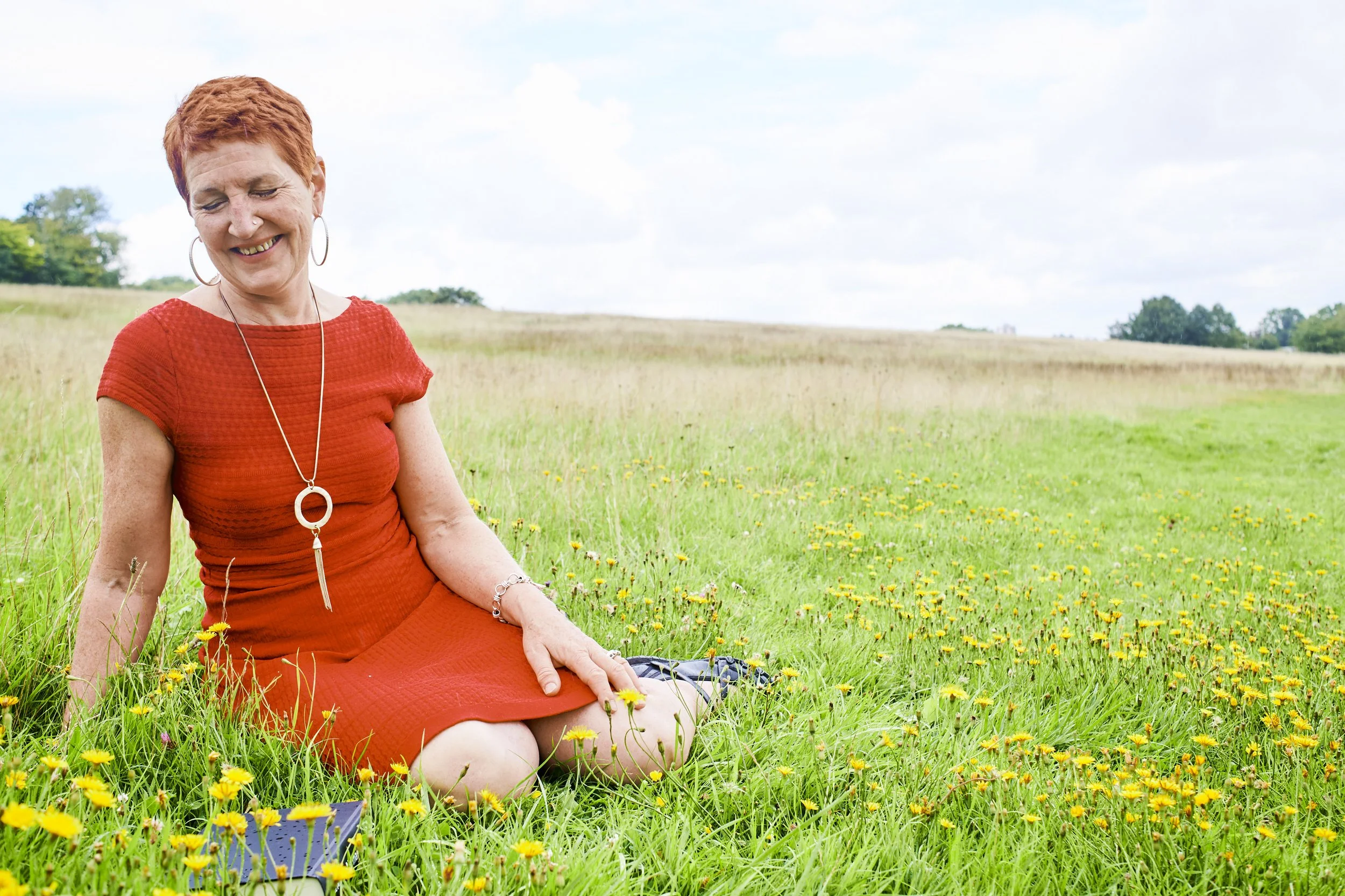 Woman in an orange dress smiling as she sits in a meadow of dandelions