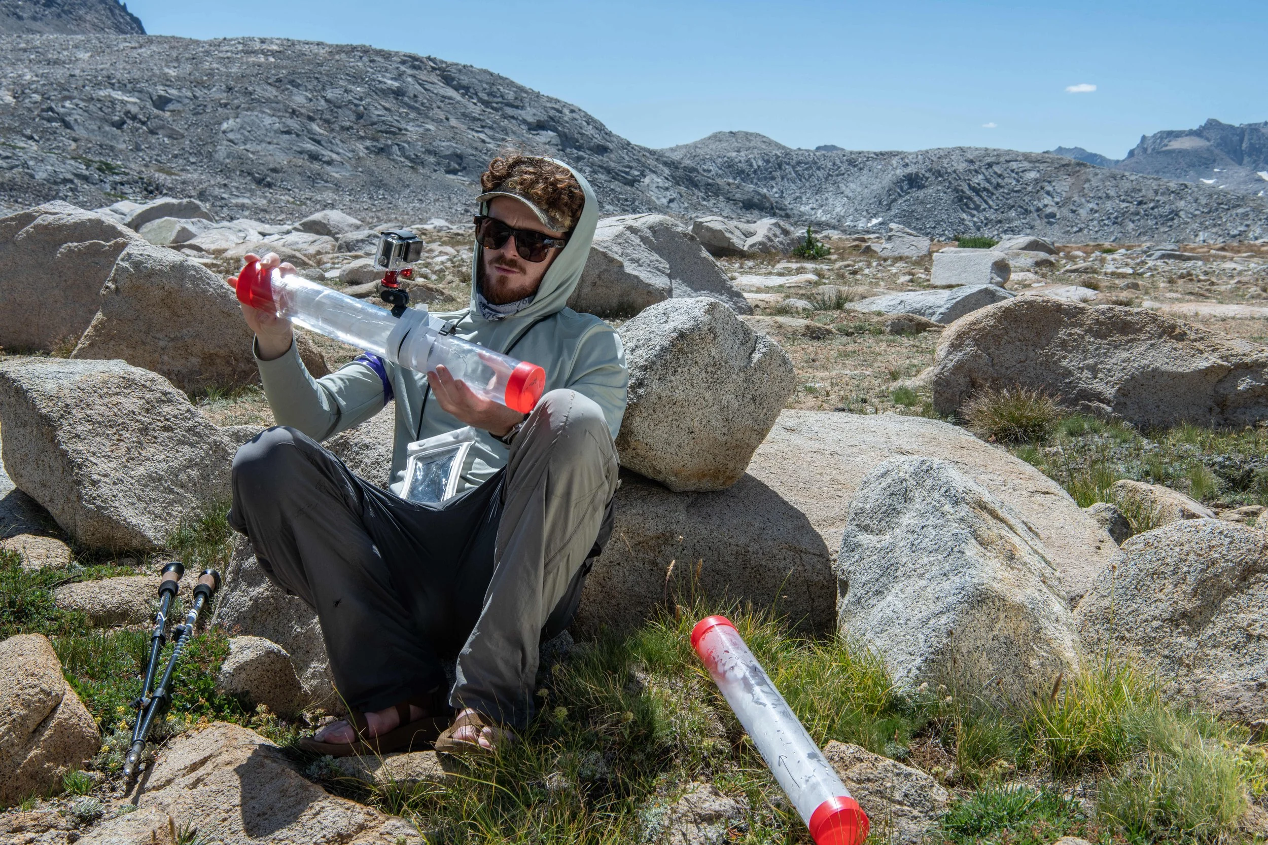 Jack holds and examines a plastic sediment core tube while sitting against a rock in the alpine Sierra Nevada