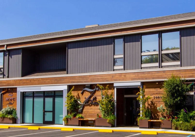 The front of 7 Stars Holisitic Healing Center. A building with wood paneling, a 7 Stars logo, and a front door with frosted glass. The parking lot is in front of the door.