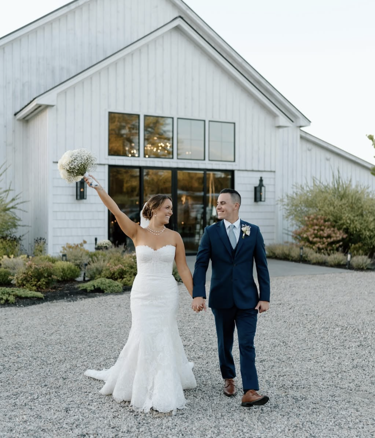 wedding couple holding hands in front of white barn wedding venue