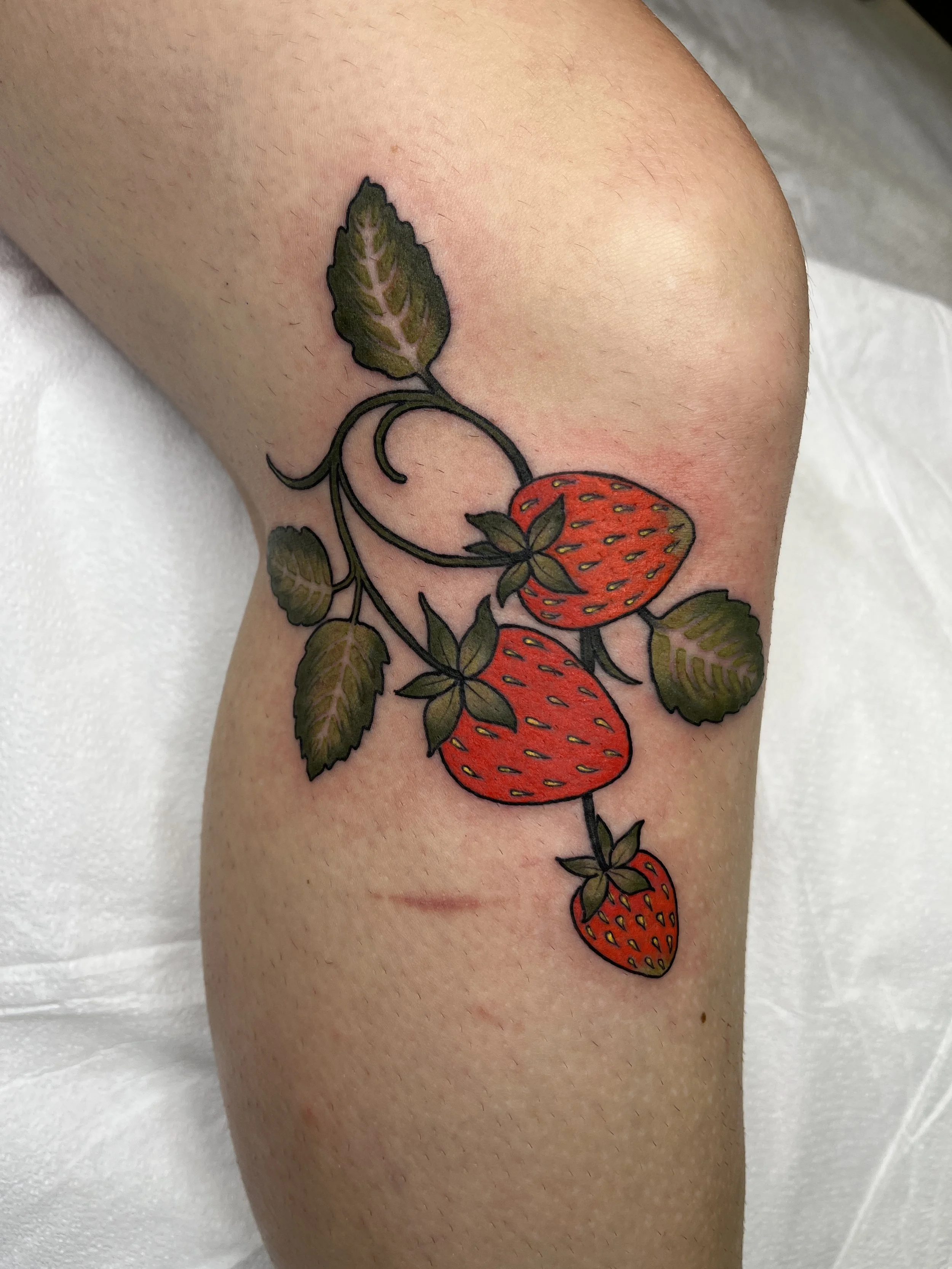 Tattoo of three strawberries with green leaves and vines on a person's upper arm.