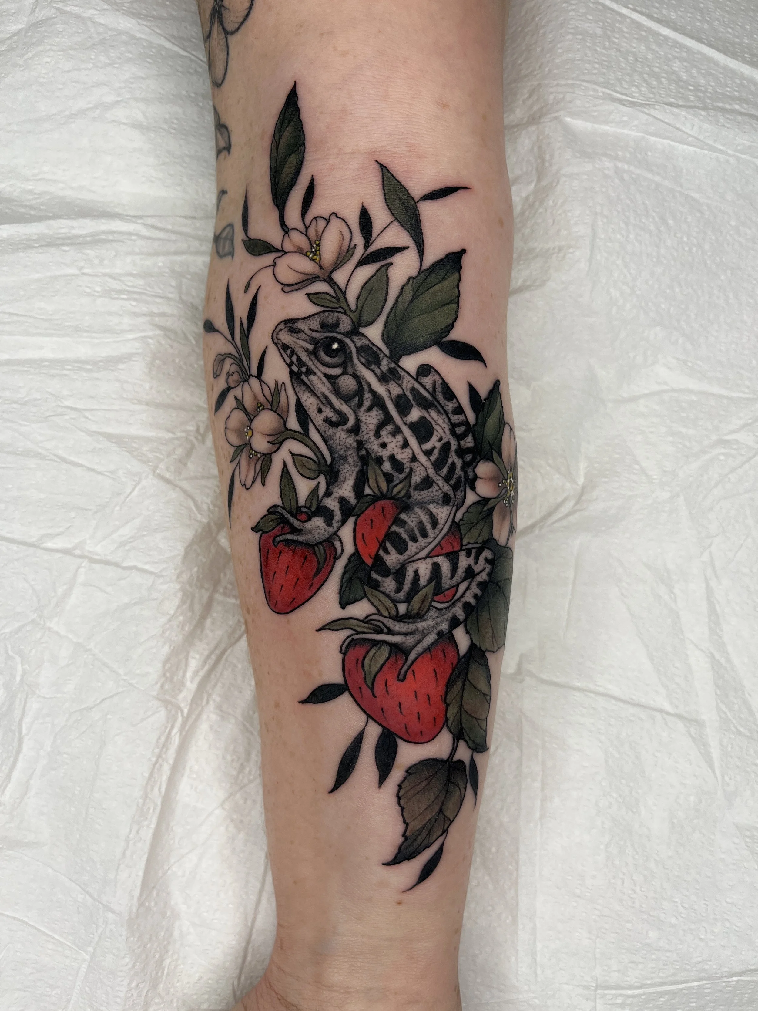 Tattoo of a snake intertwined with strawberries and surrounded by green leaves and small white flowers.