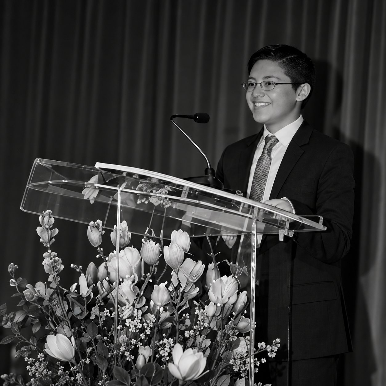 Young speaker giving speech behind clear podium with flowers.png