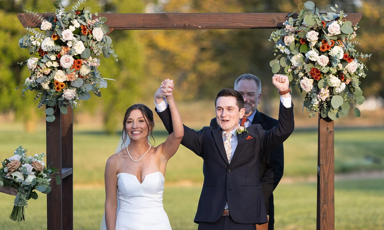 Bride and groom celebrating getting married outdoors with a floral arch designed by The Flower Lab in St. Louis.