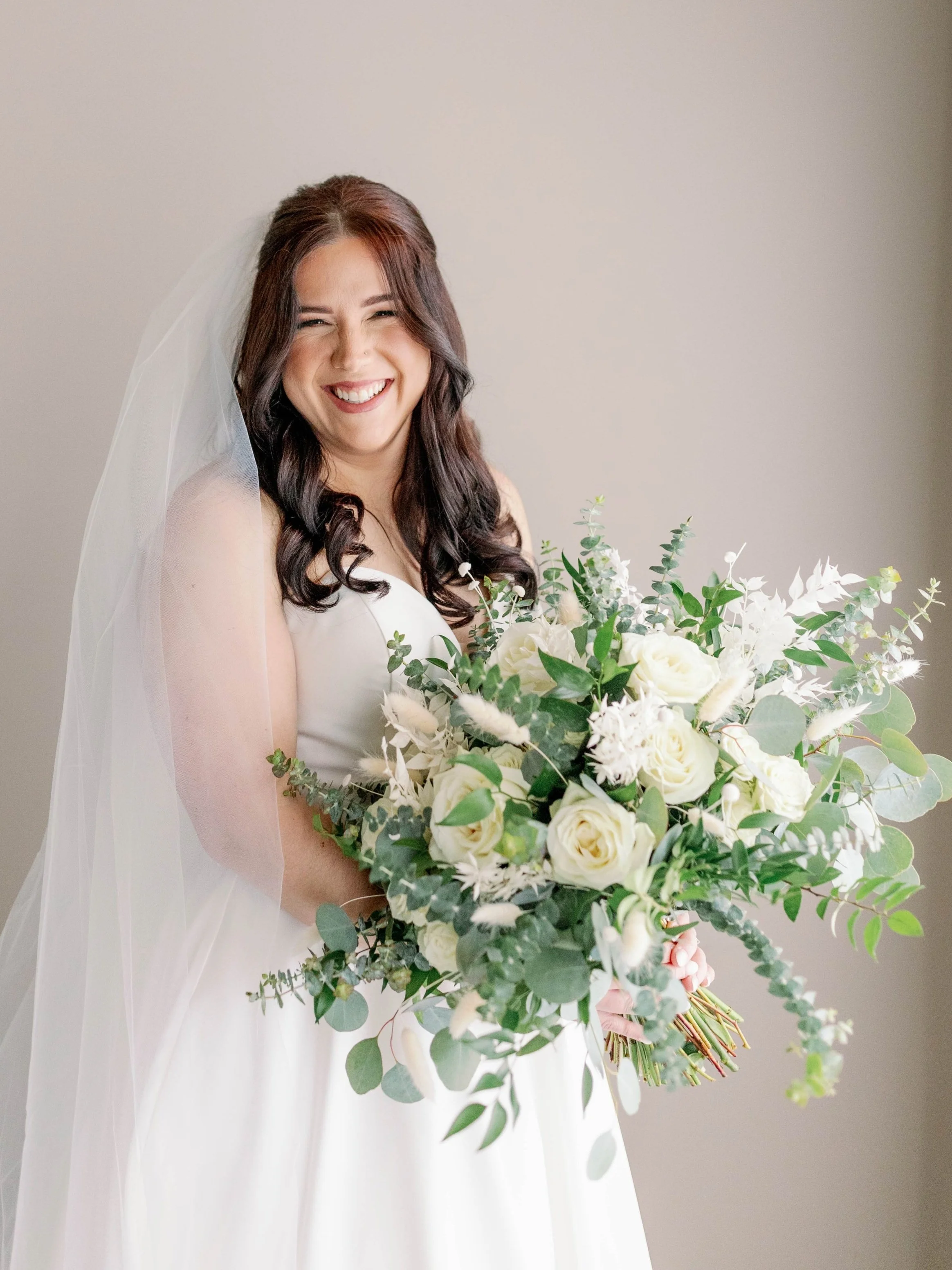 Smiling bride with while veil holding a bouquet from White Garden Collection with Boho accents added.