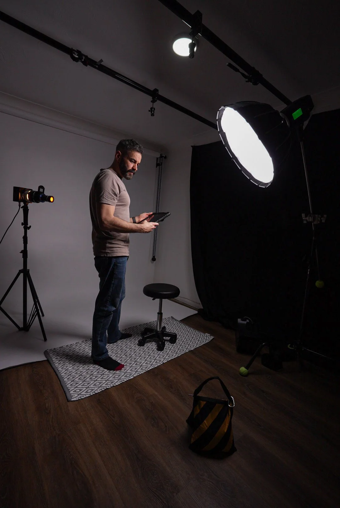 A man standing in a photography studio, looking at a tablet, with professional lighting equipment and a black backdrop.