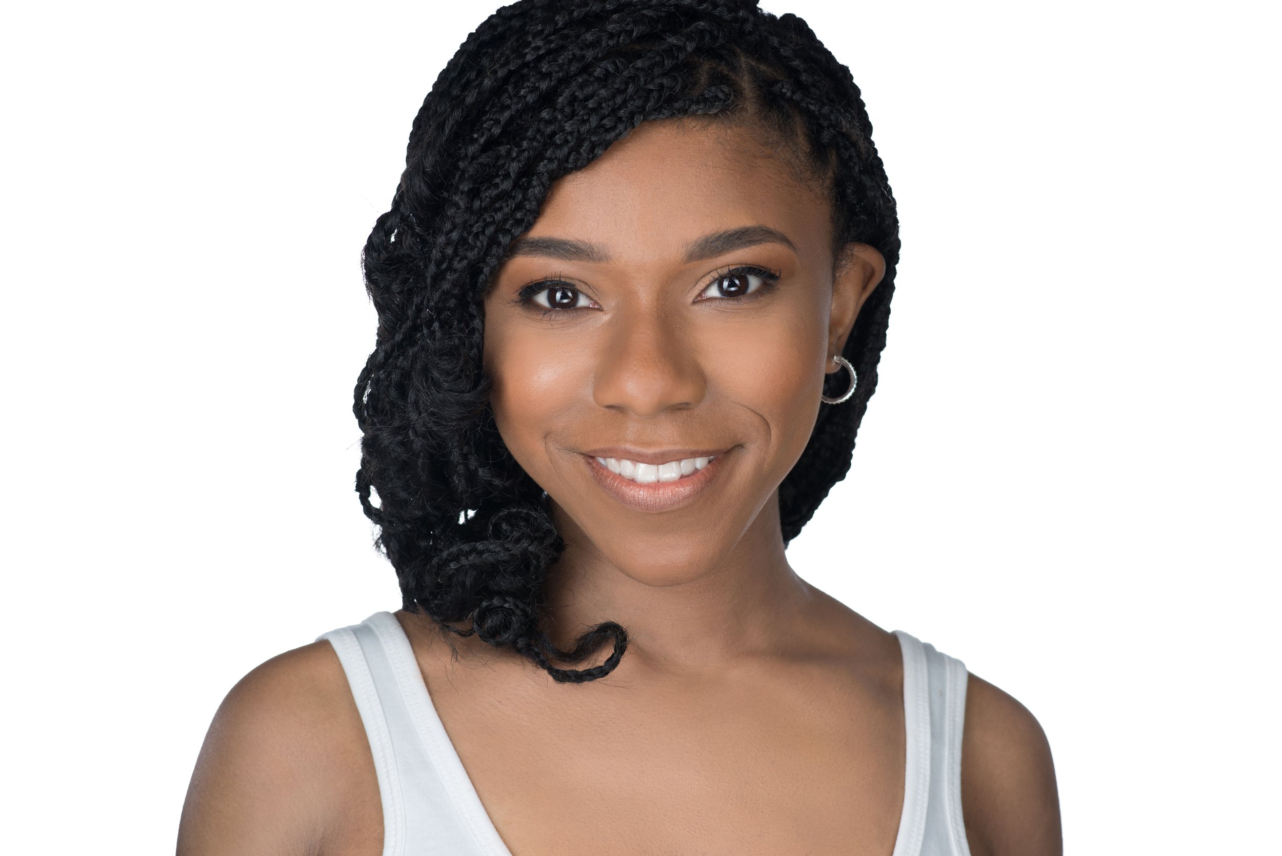 Close-up portrait of a young woman with braided black hair, smiling, wearing a white sleeveless top, and small hoop earrings, against a white background.