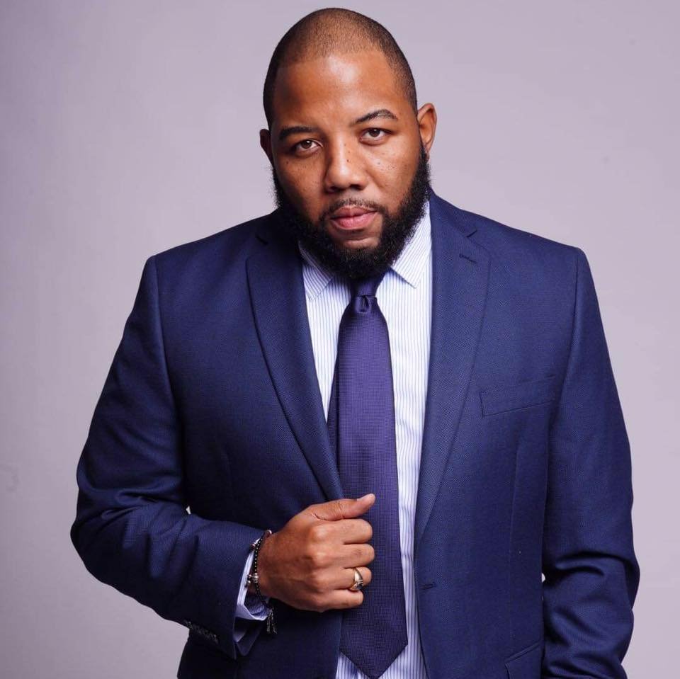 A man in a blue suit and tie posing against a plain gray background.