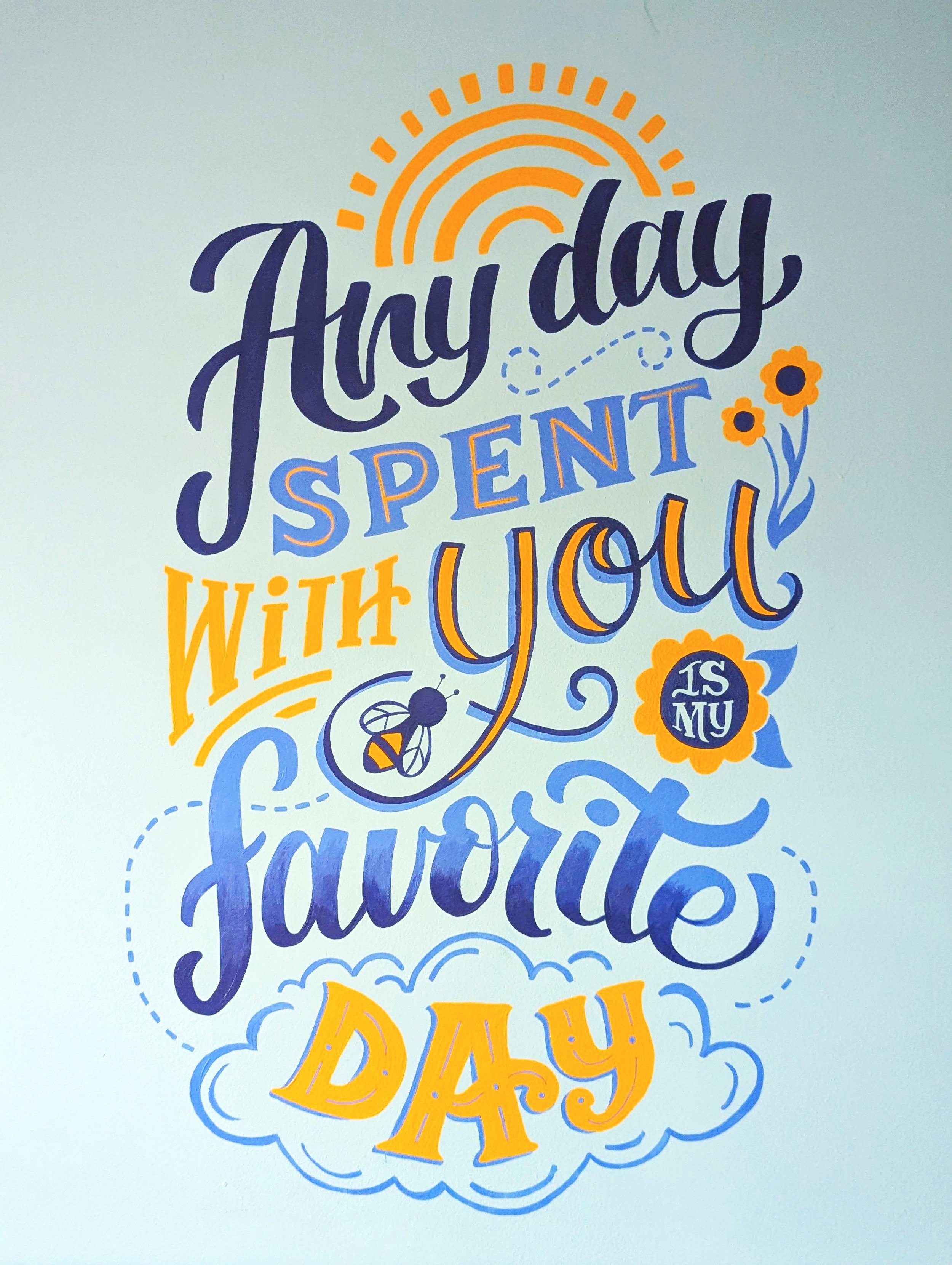 Nursery wall mural art with text "Any day spent with you is my favorite day," featuring decorative fonts, flowers, a bee, a sun, and clouds.