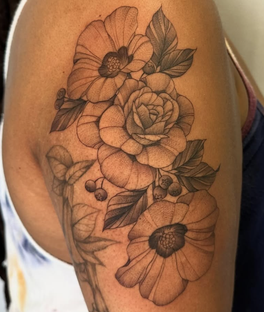 A detailed black and gray floral tattoo featuring large poppies, roses, and leaves on a person's upper arm.