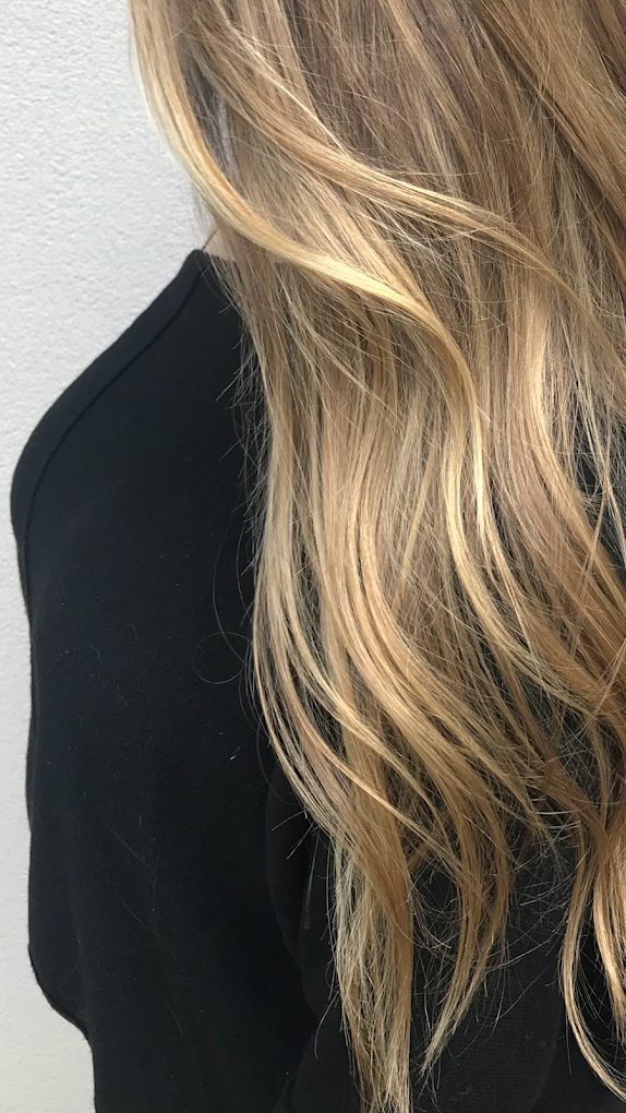 Close-up of a woman's long, wavy, blonde hair and part of her black top against a light gray background.