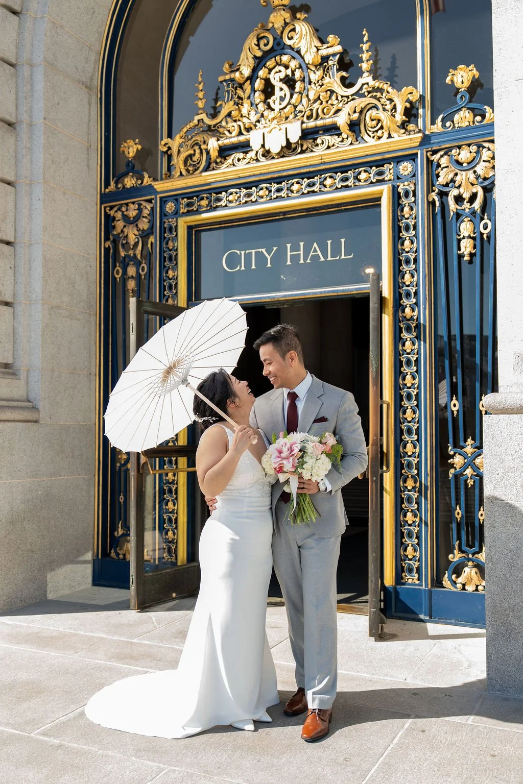 bride and groom smiling at entrance for San Francisco City Hall wedding photography