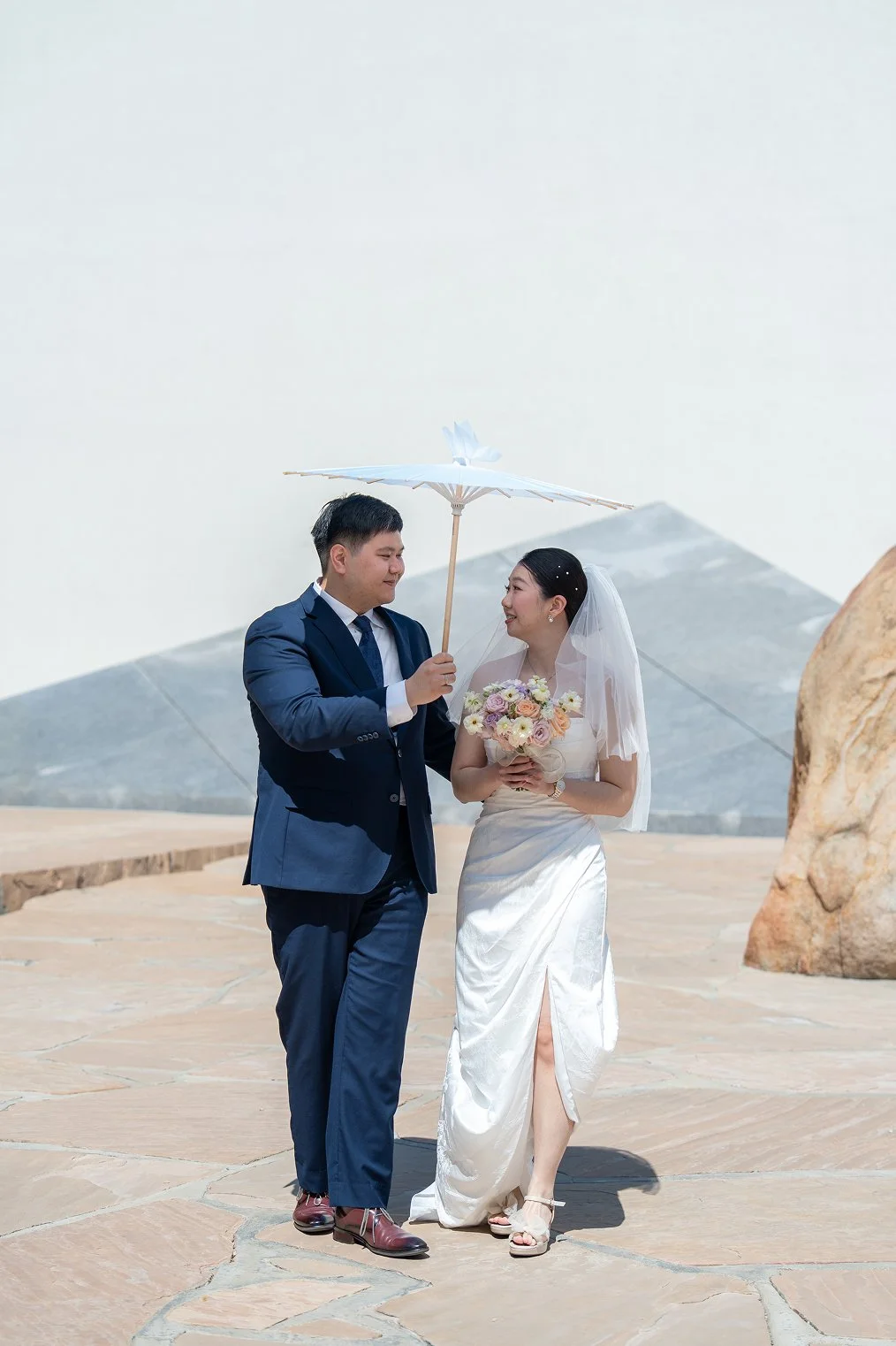 The groom holds a parasol for his bride while taking Orange County wedding photos