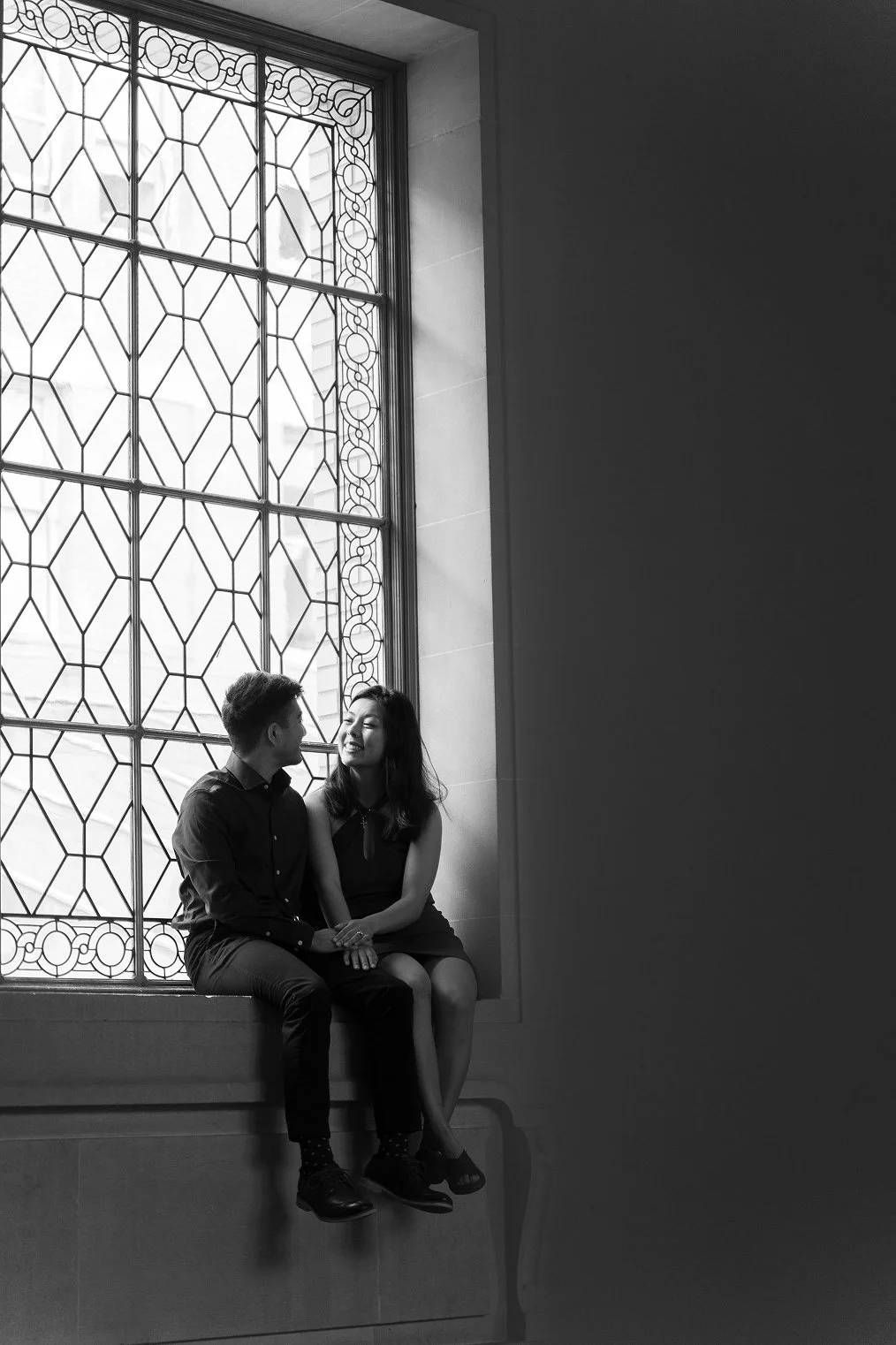A couple sits by a window for their San Francisco City Hall engagement photos.