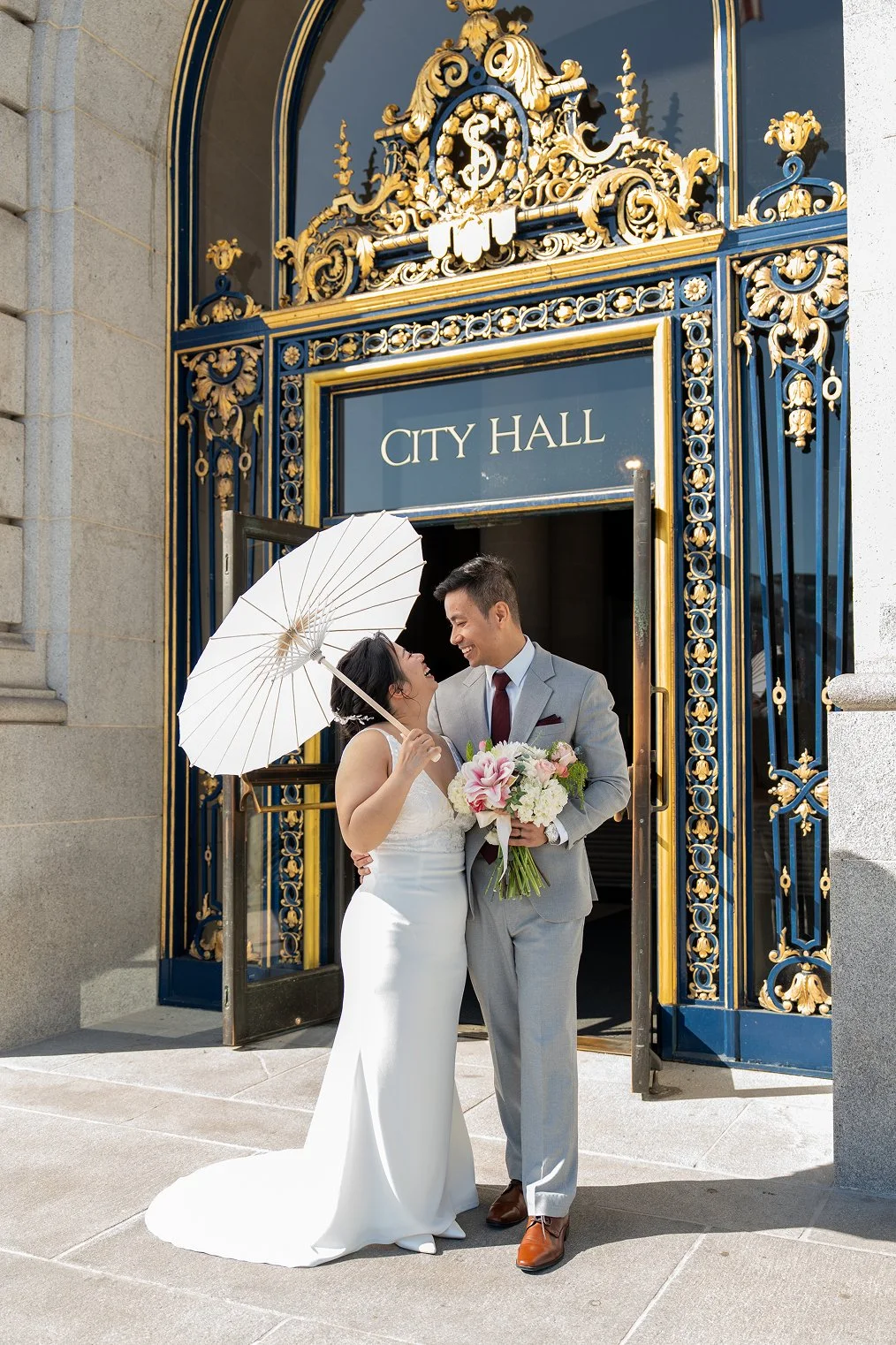 A couple smiles at the entrance for San Francisco City Hall wedding photos.