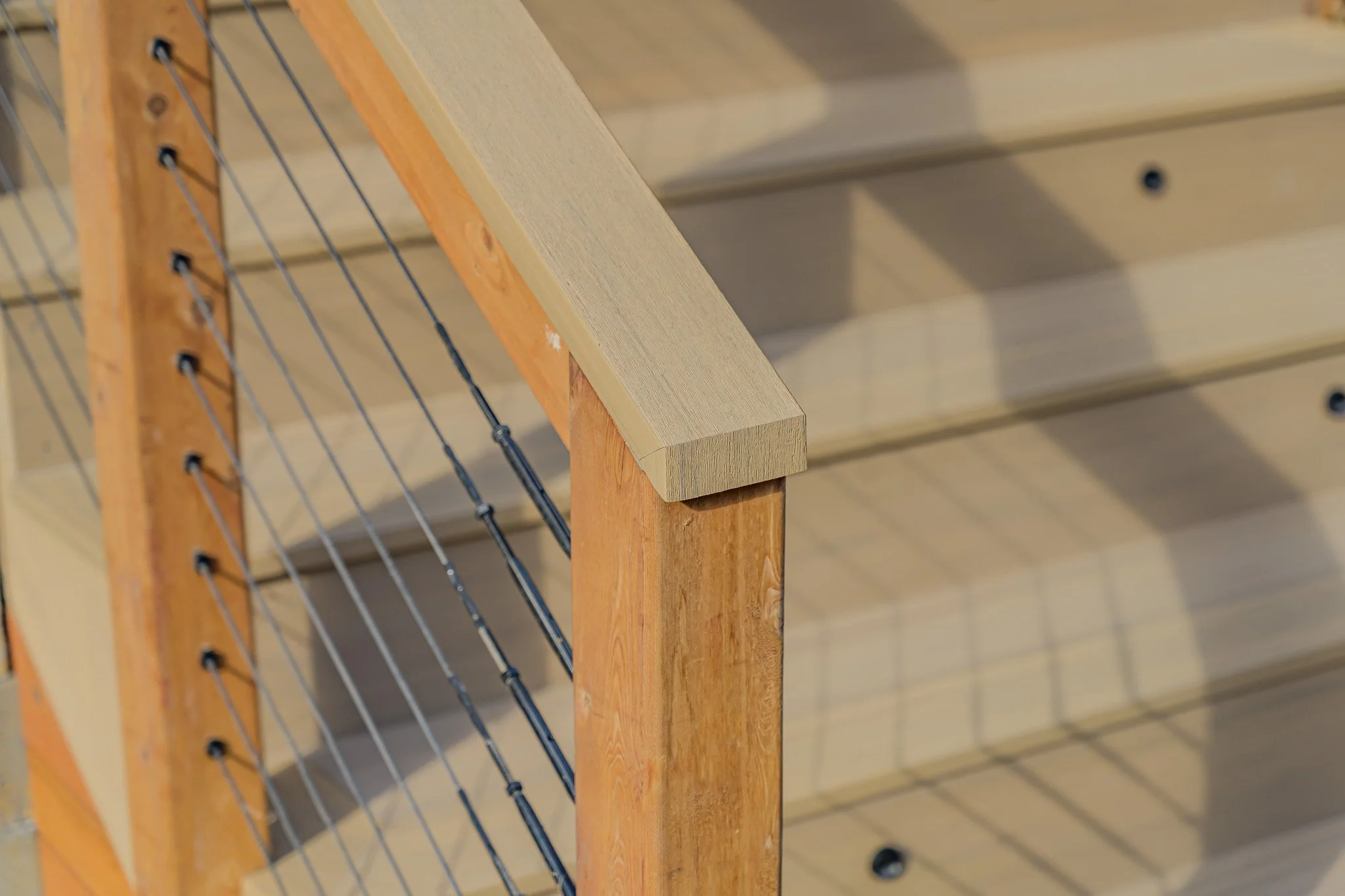 Close-up view of a wooden staircase handrail with metal wires, showing the connection detail at the corner.