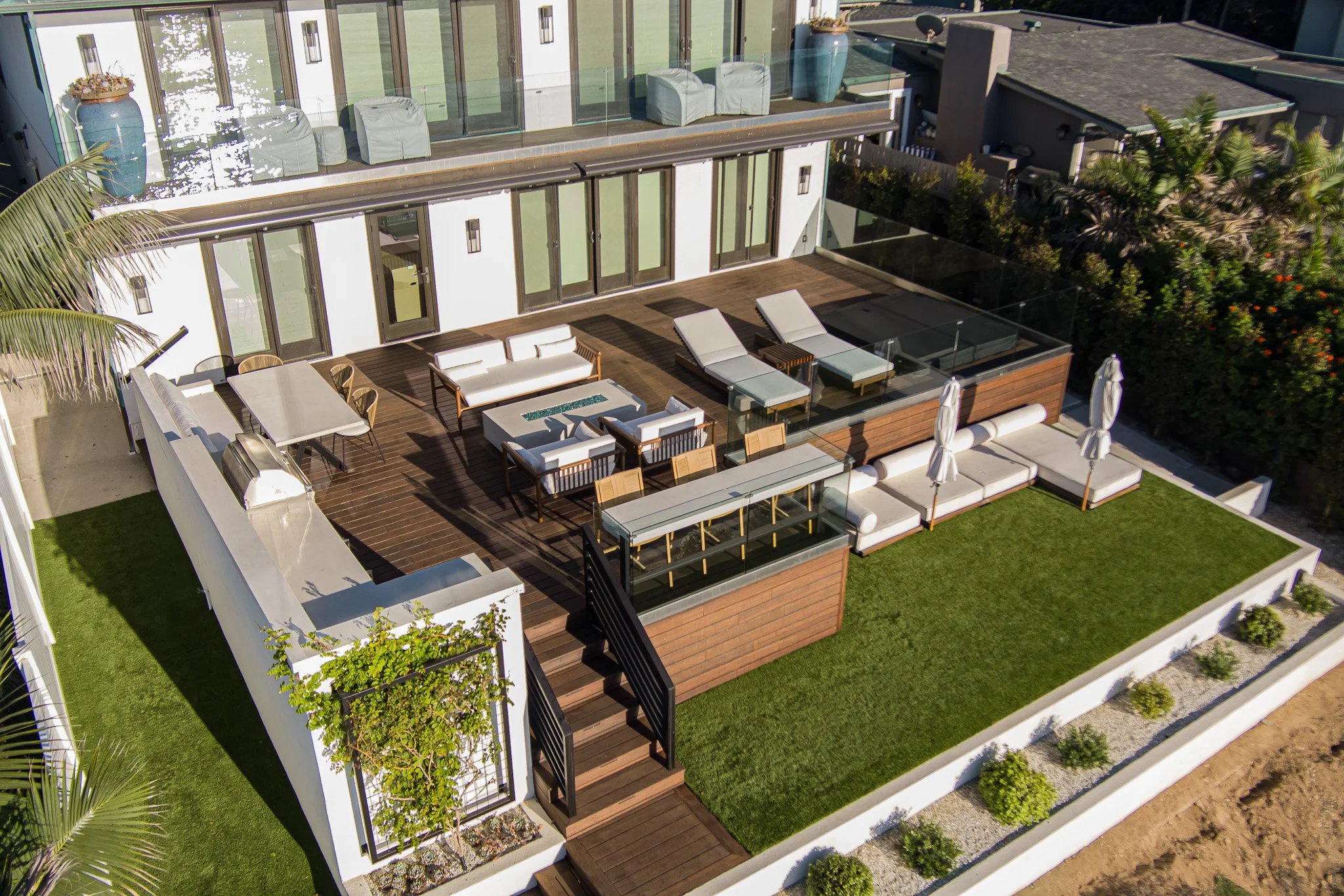 Aerial view of a modern house's outdoor patio with seating area, lounge chairs, dining table, and lush greenery surrounding the area.