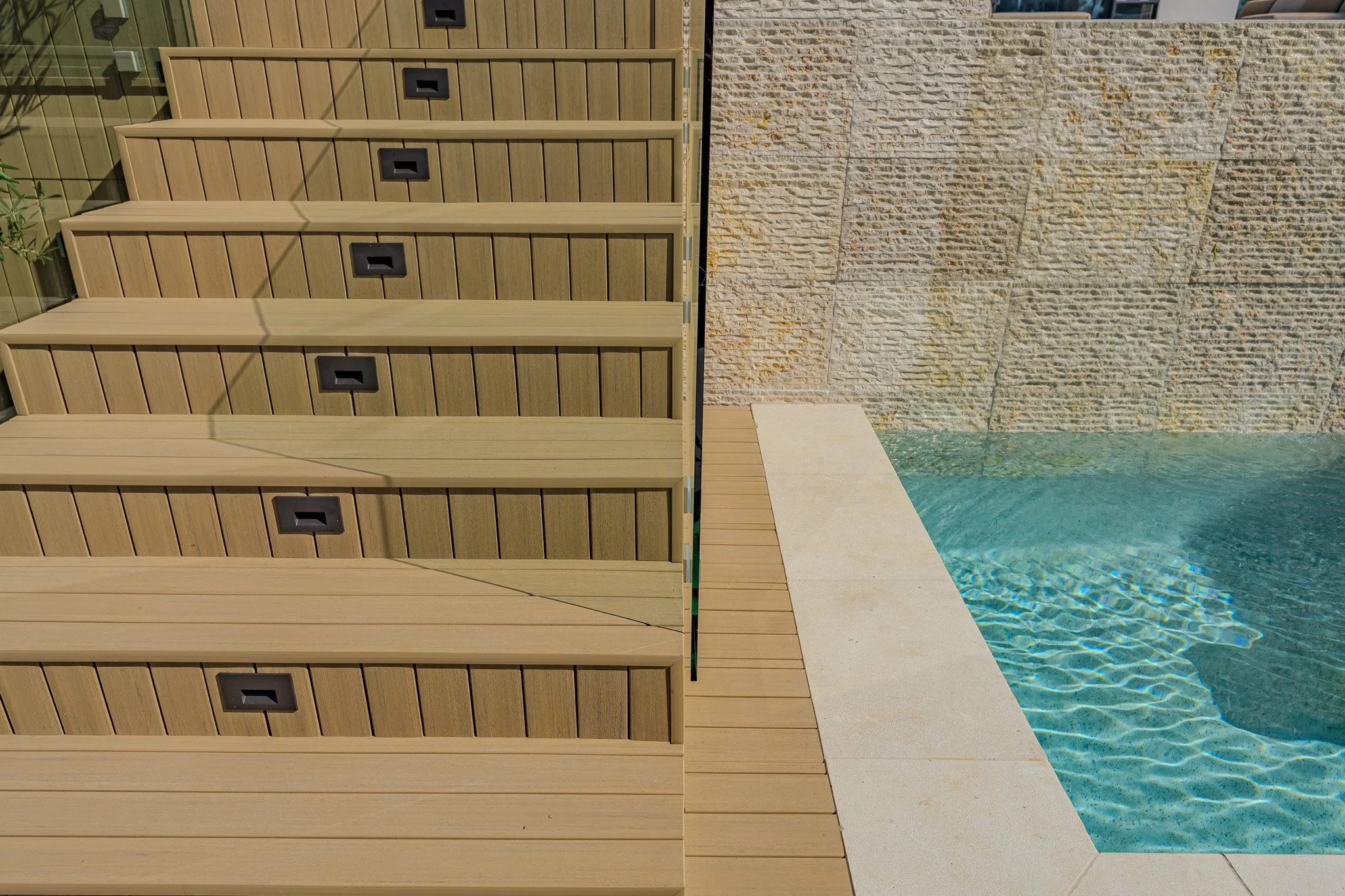 View of a poolside area with a wooden fence, a stone wall, and pool water visible on the right side.