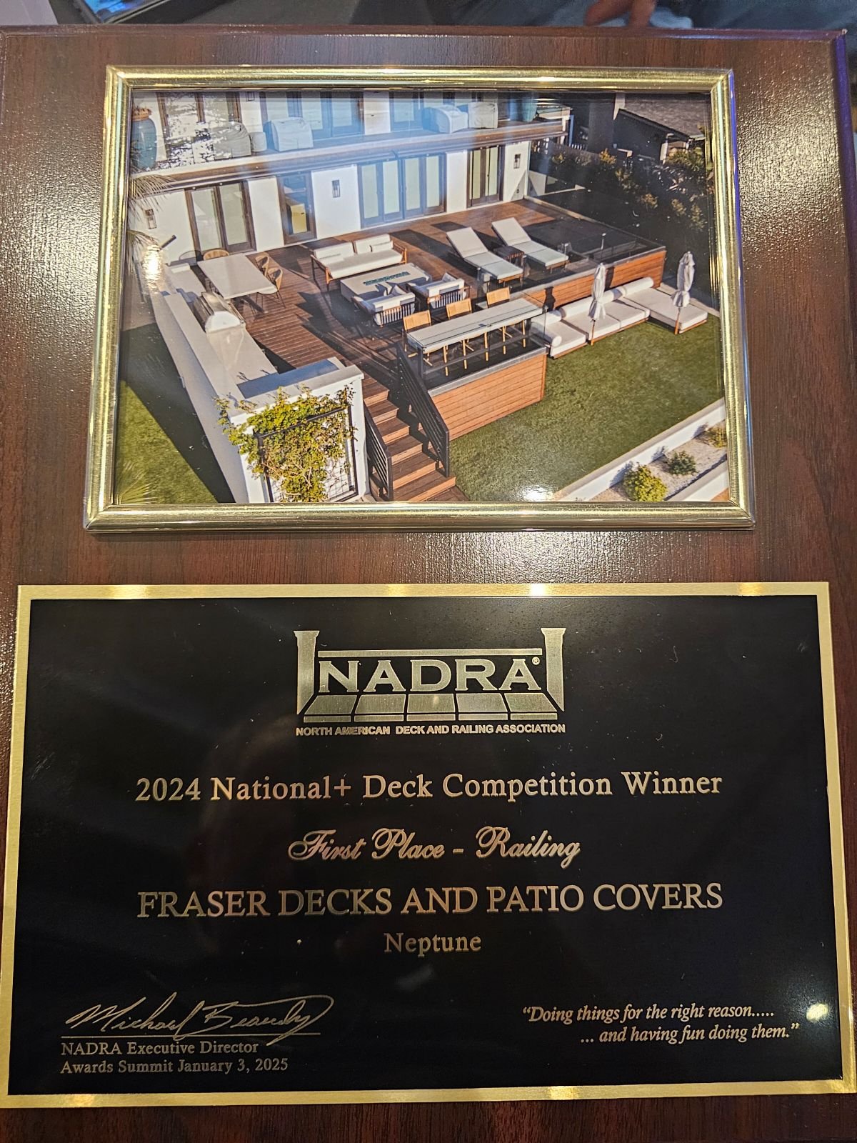 Plaque and framed photo from the NADRA North American Deck and Railing Association awards, showing a rooftop patio with furniture, grass, and a building exterior, awarded for first place in railing in 2024.