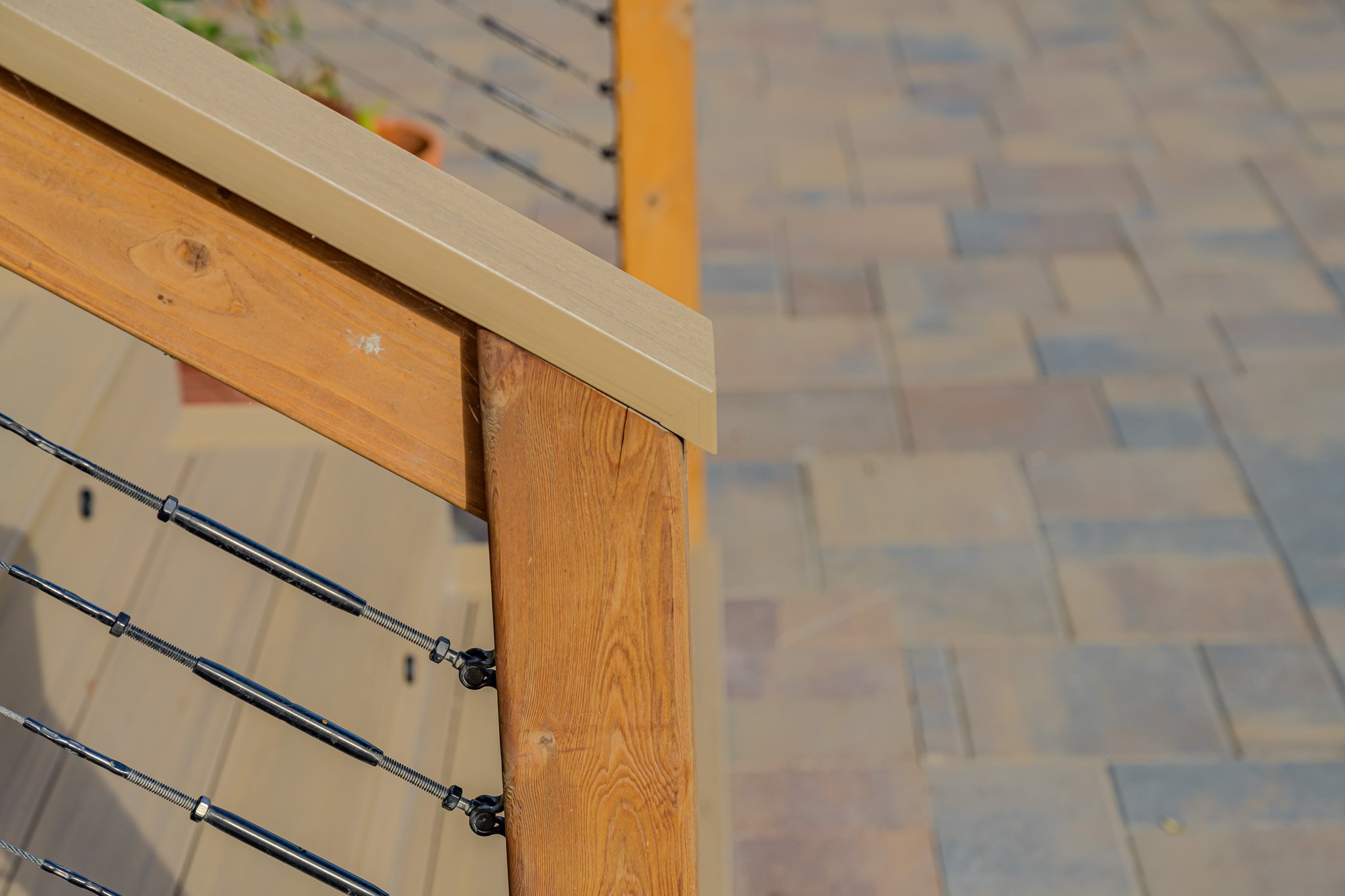 Close-up of a wooden bench with metal and rope safety wires attached, overlooking a paved outdoor area.