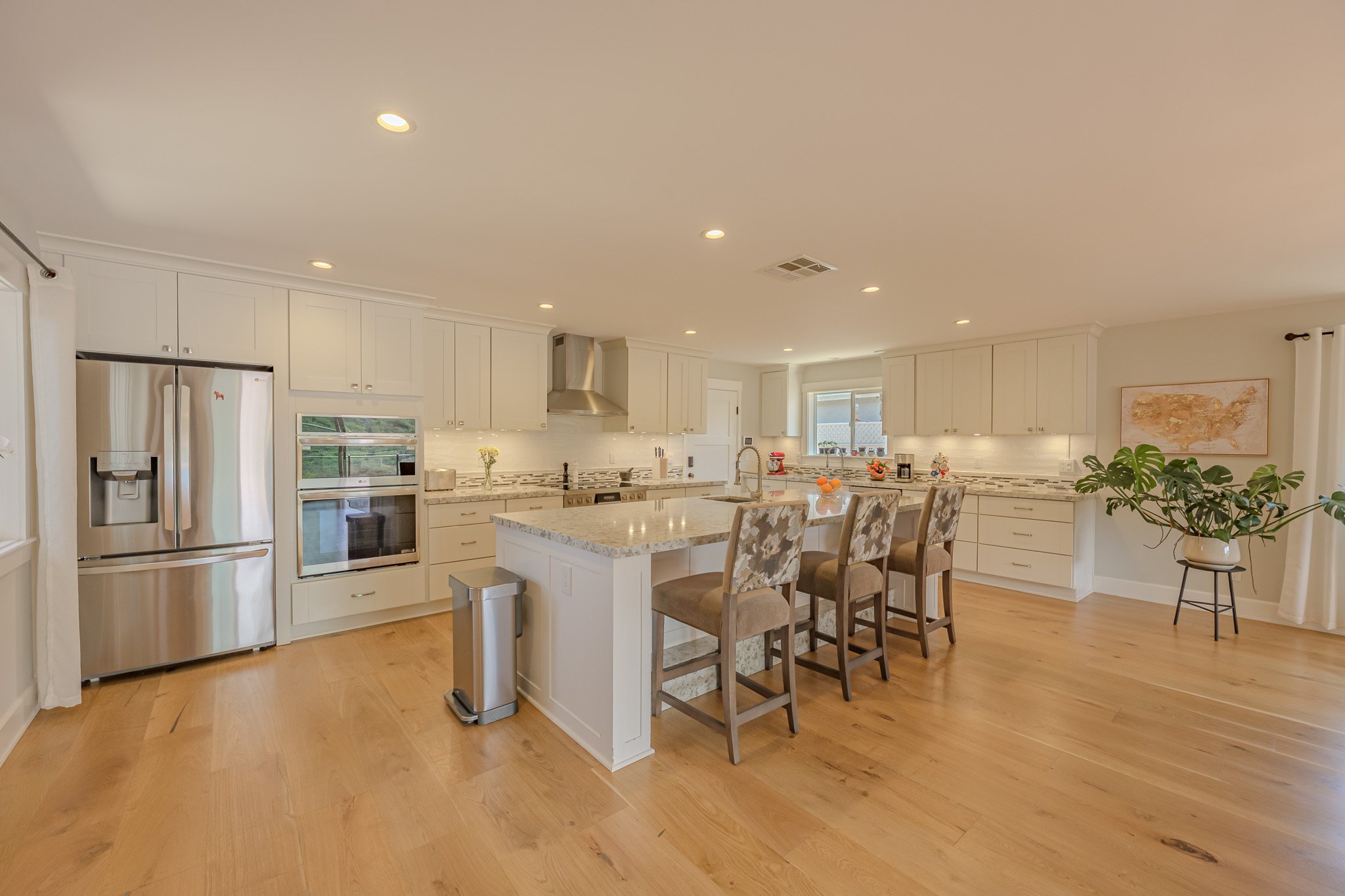 A spacious modern kitchen with white cabinets, stainless steel appliances, a large island with a granite countertop, barstools, and a wooden floor.