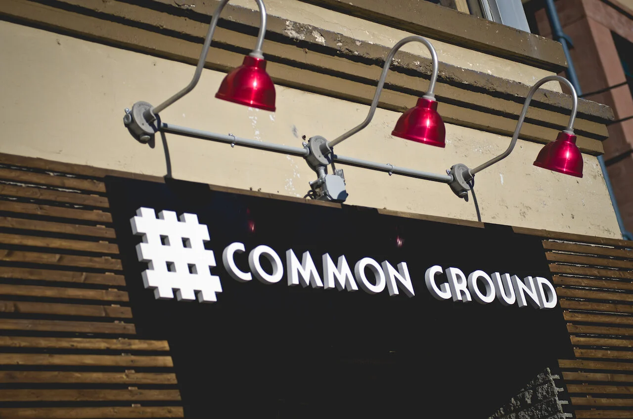 Signboard with the text '#COMMON GROUND' illuminated by three red lights above it.