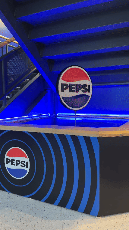 Pepsi logo on a circular sign and on a display with blue neon lighting at a Pepsi promotional booth.