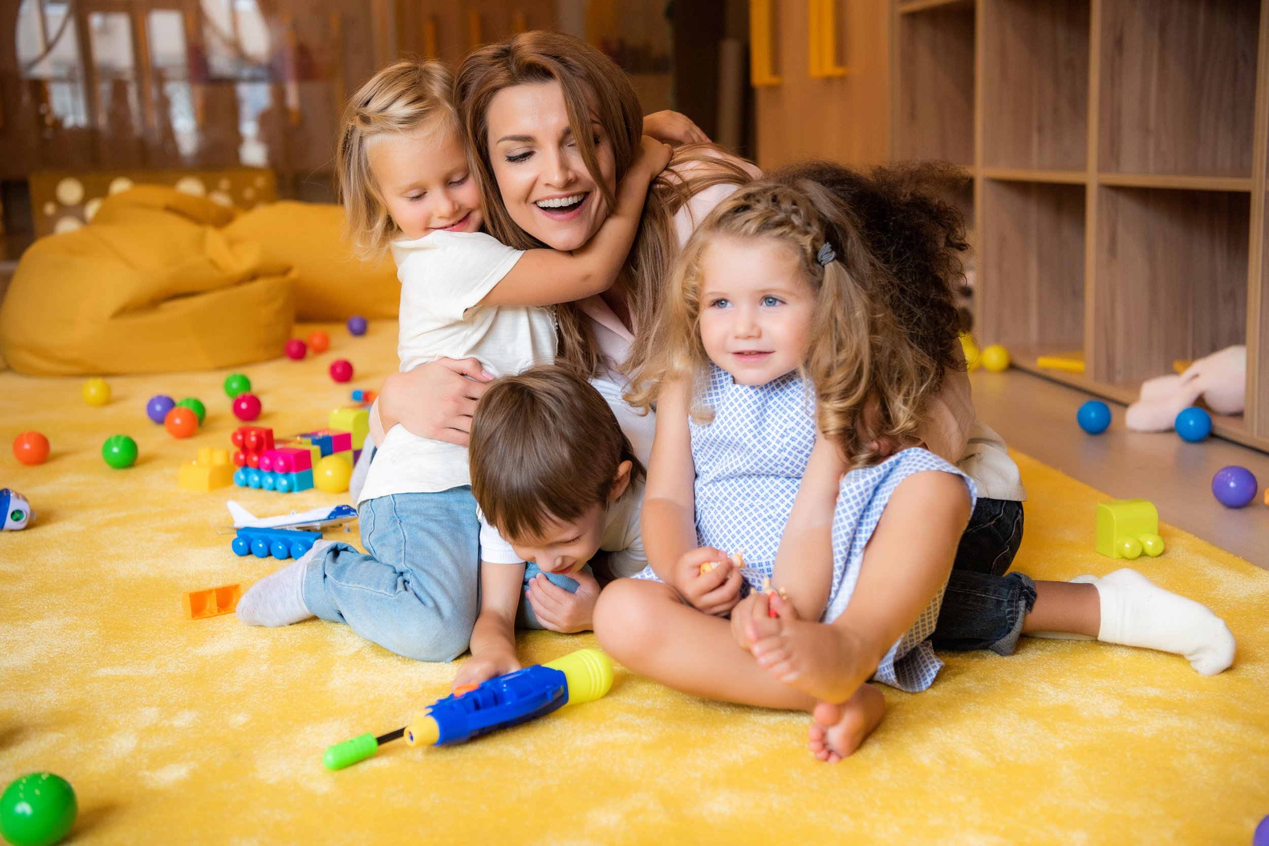 smiling-woman-hugging-children-in-playroom-setting-2026-09-22-21-29-32-utc.jpg
