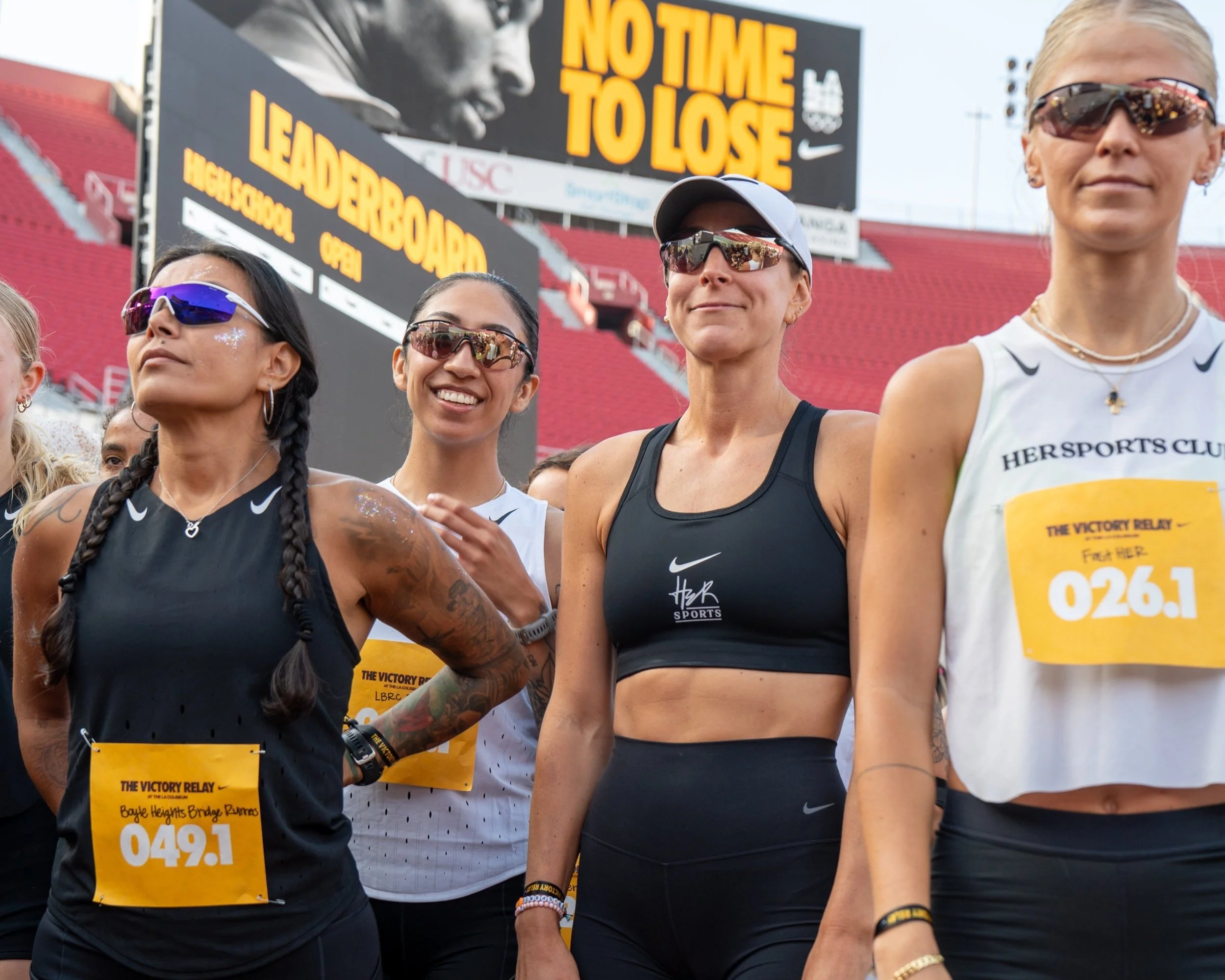 HER Sports athletes gathered at a race event in a stadium, ready to compete and train.