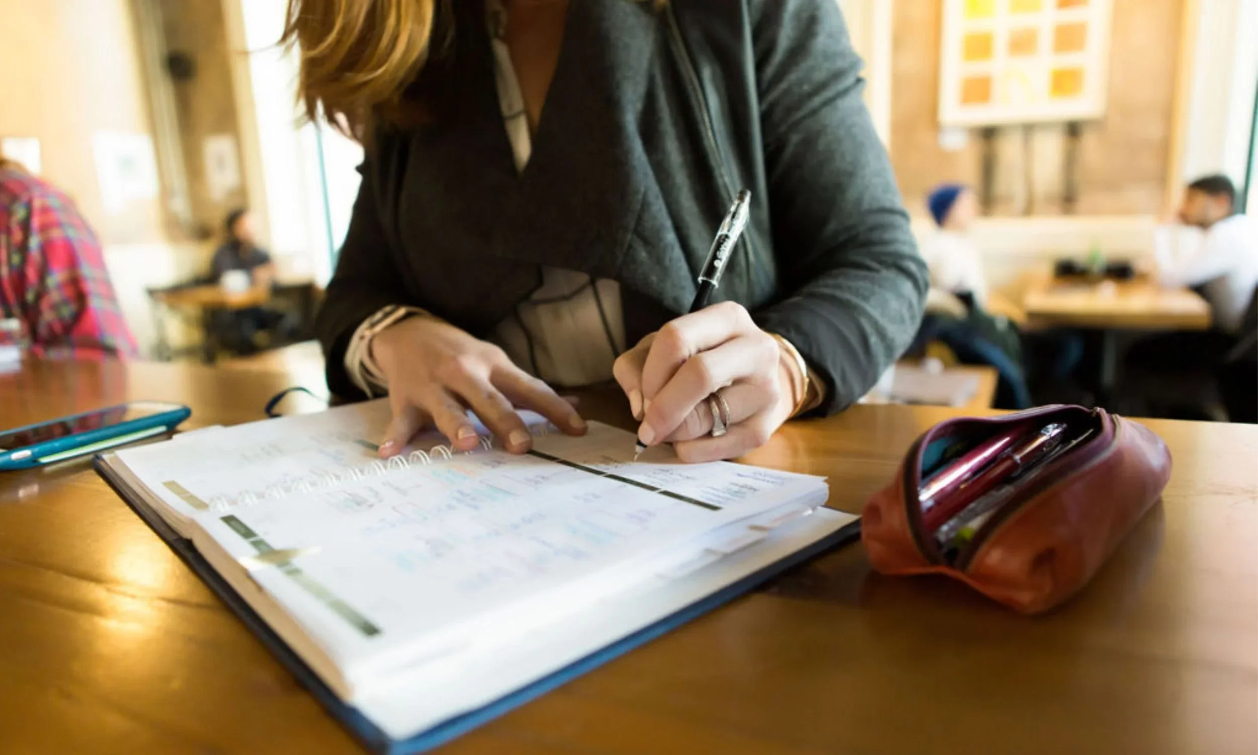 A woman using a color-coded daily planner and erasable pens to manage ADHD executive functioning and daily tasks in a cafe.