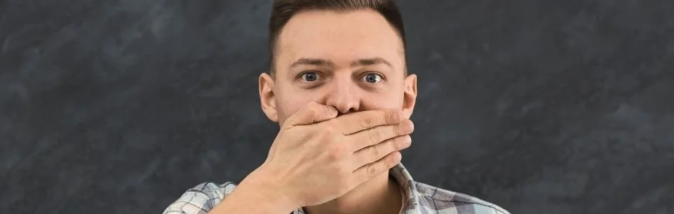 Man covering his mouth in sudden realization, representing awareness of interrupting behavior in ADHD