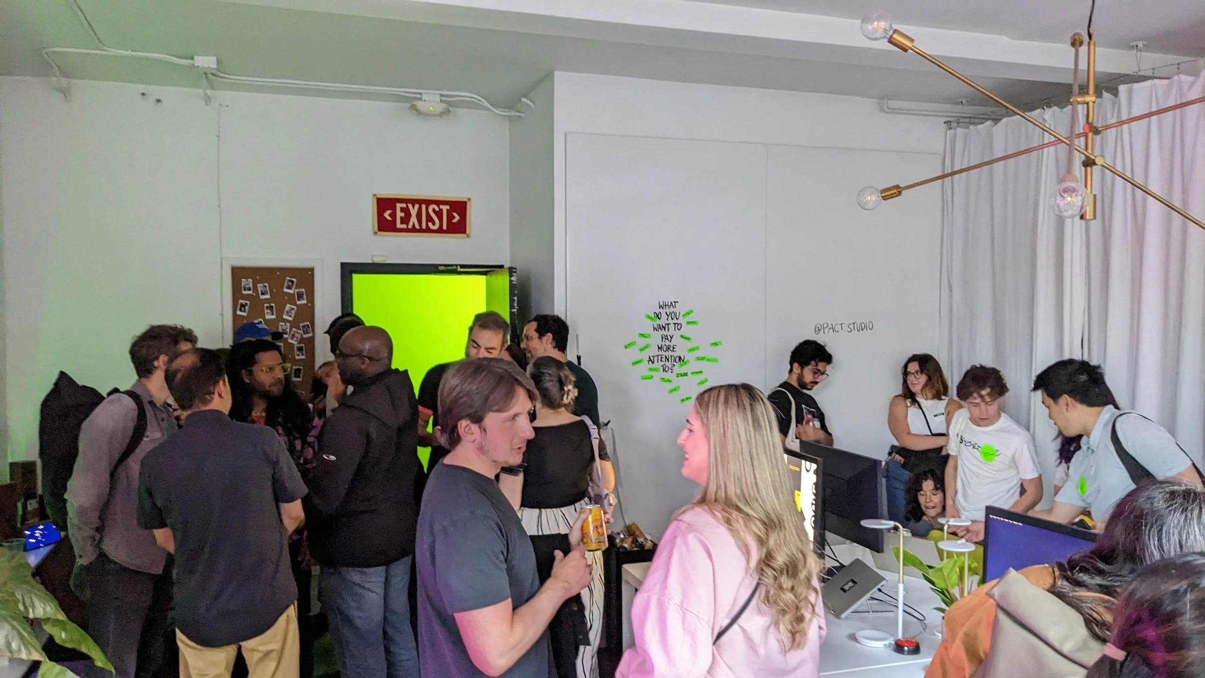 Crowd of visitors and designers mingling inside Pact Studio during San Francisco Design Week, gathered around desks and computer monitors in the small Mission District studio.