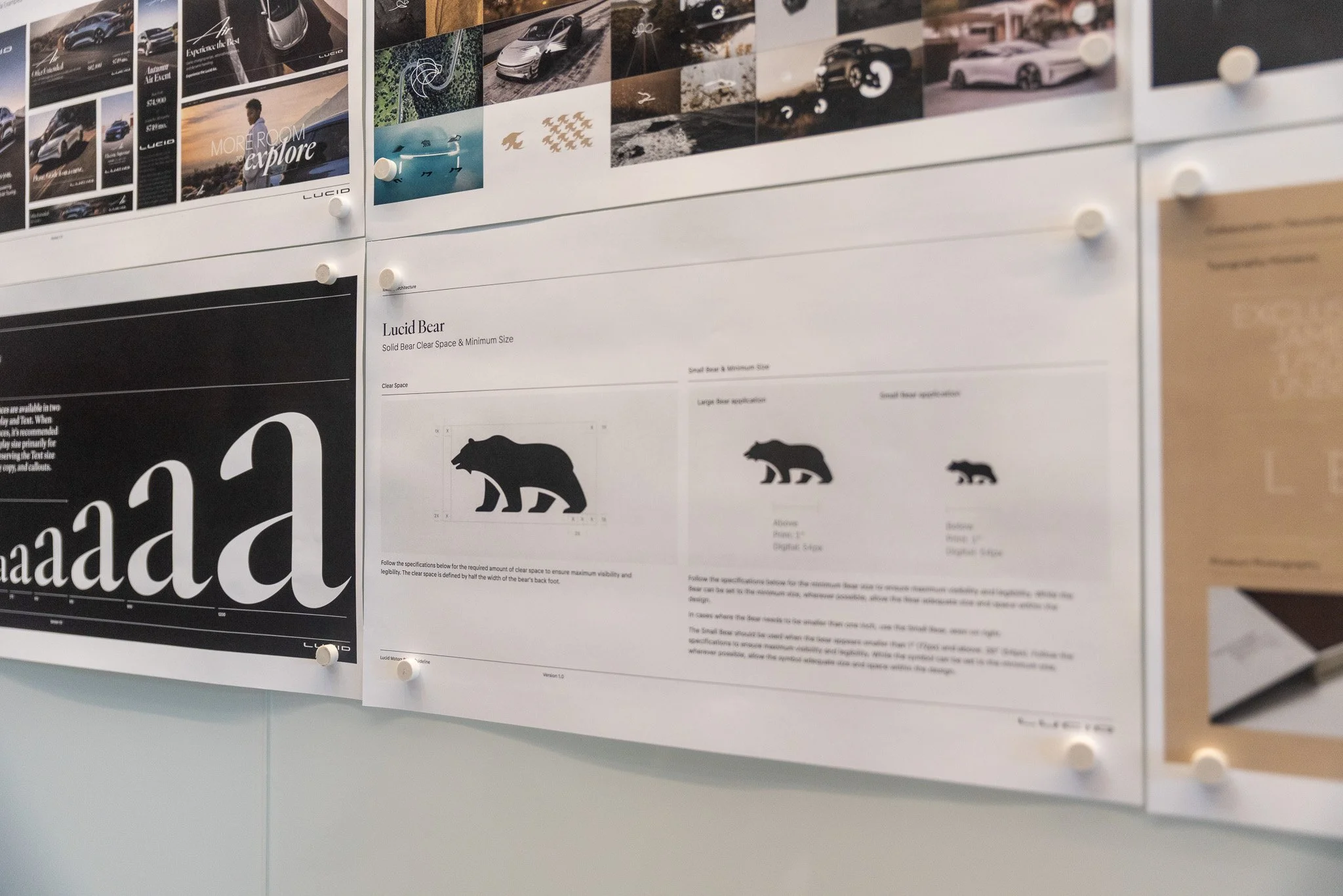 A close-up of printed brand guideline sheets pinned to a white wall, displaying the black silhouette of the Lucid Bear logo with clear space measurements, minimum size requirements, and typography samples.