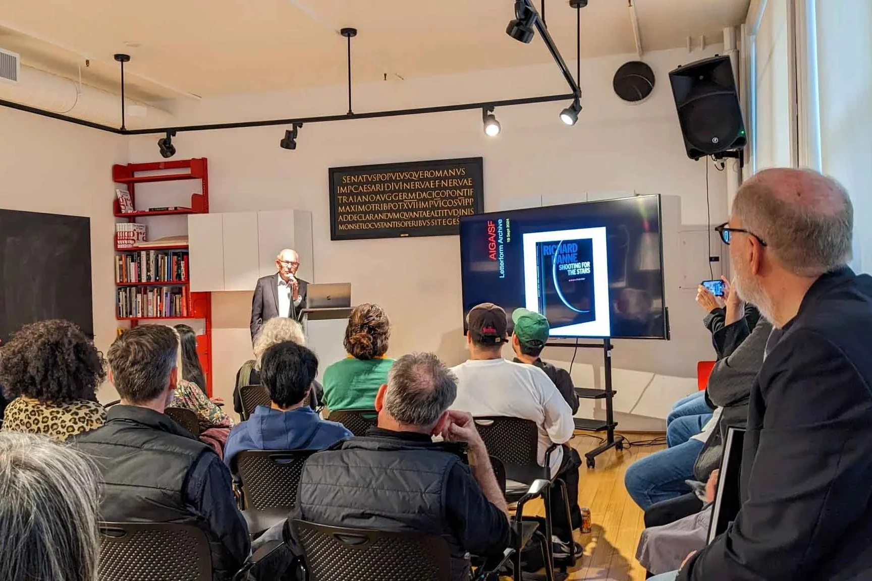 Richard Danne speaks to a packed audience at Letterform Archive in San Francisco, presenting slides from his book Shooting for the Stars during a lecture on his career in graphic design.