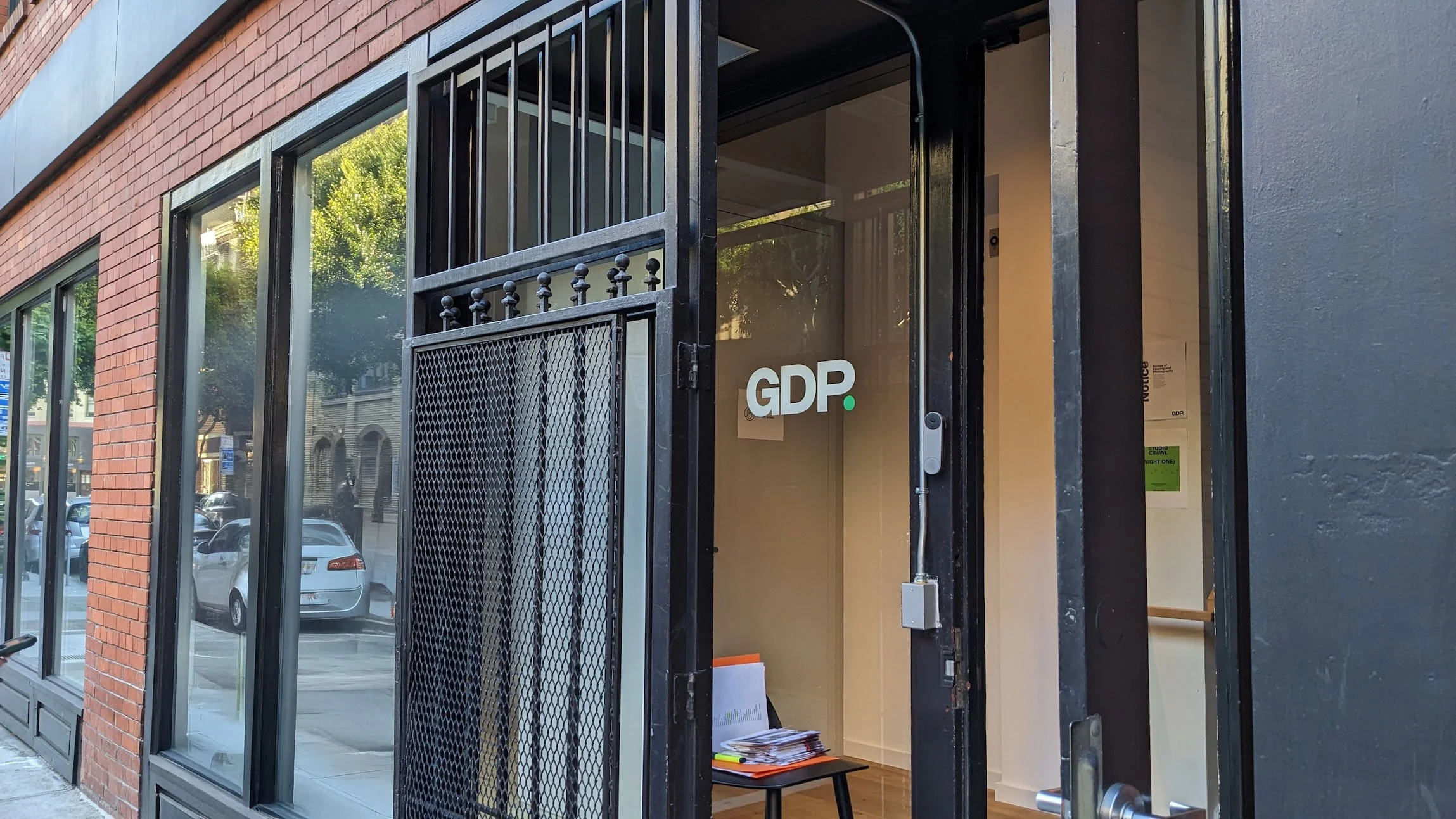 Glass door entrance to the Godfrey Dadich Partners studio, showing the “GDP.” logo on the door and a small table with booklets inside, along a brick-lined street in San Francisco’s Jackson Square.