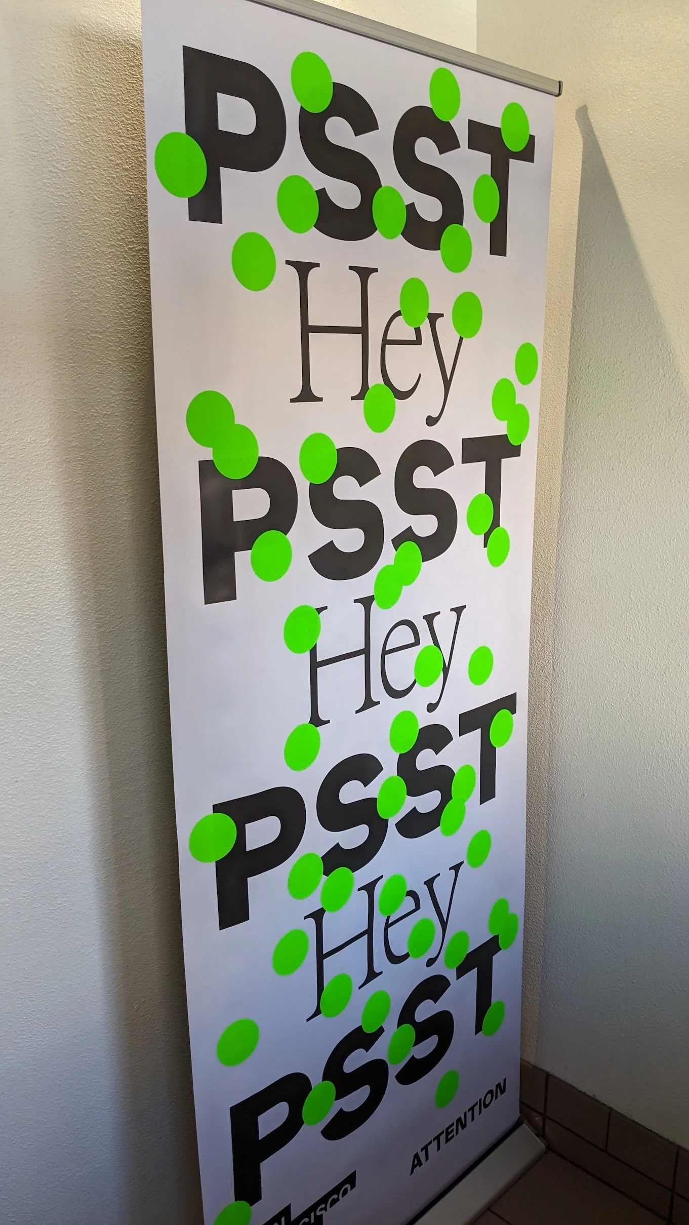 Vertical banner reading “Psst Hey Psst Hey Psst” covered with bright green circular stickers at the entrance to Pact Studio during San Francisco Design Week.