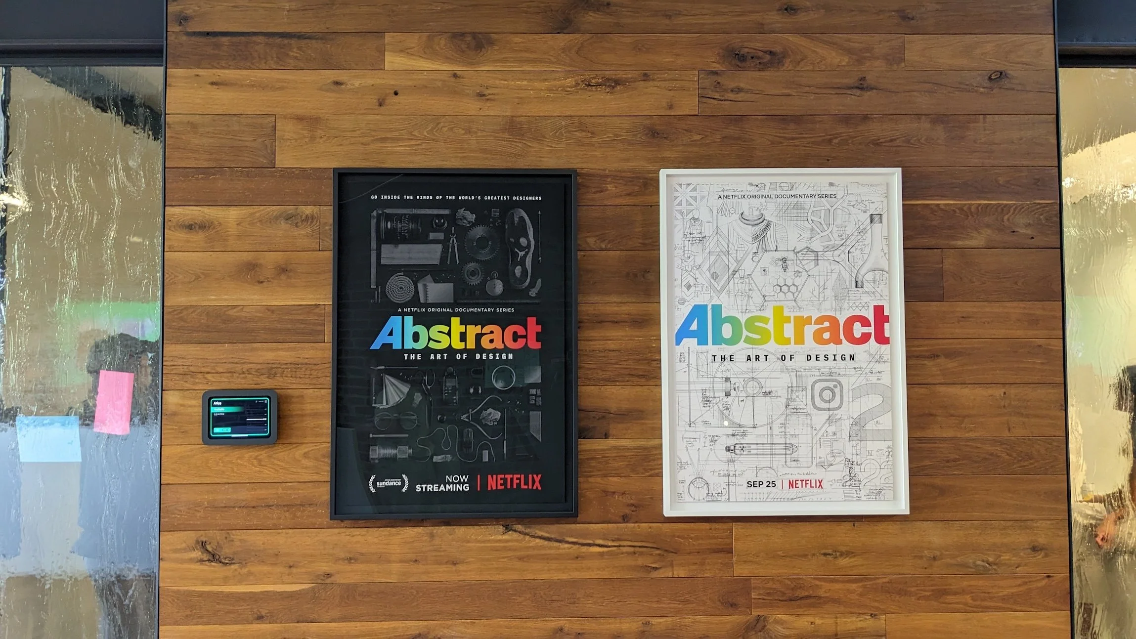 Two framed posters for Abstract: The Art of Design mounted on a wooden wall, one in black with technical objects and one in white with line-art illustrations.