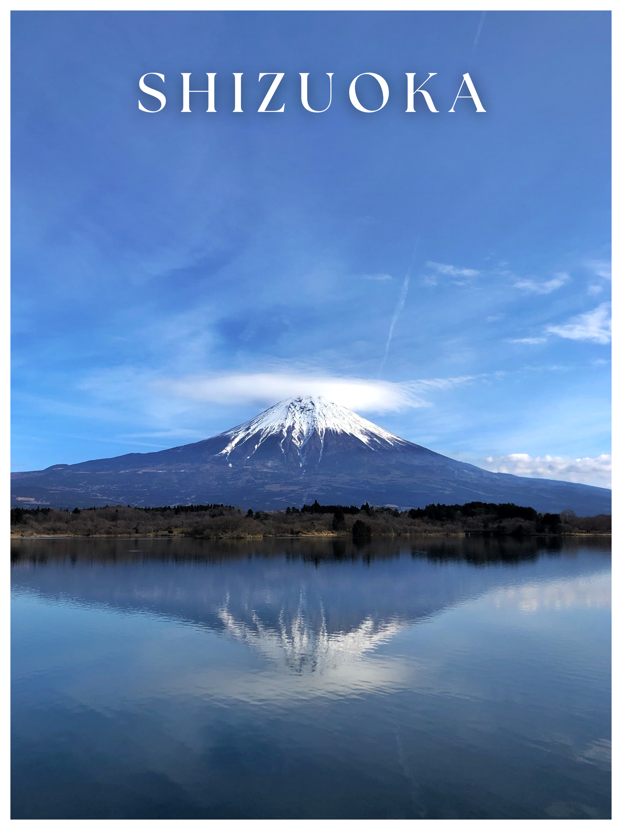 A snow-capped mountain, Mount Fuji, reflected in a lake with a forested area along the shoreline, under a blue sky with wispy clouds - found in Shizuoka, Japan - a quieter alternative to  popular, crowded Yamanashi