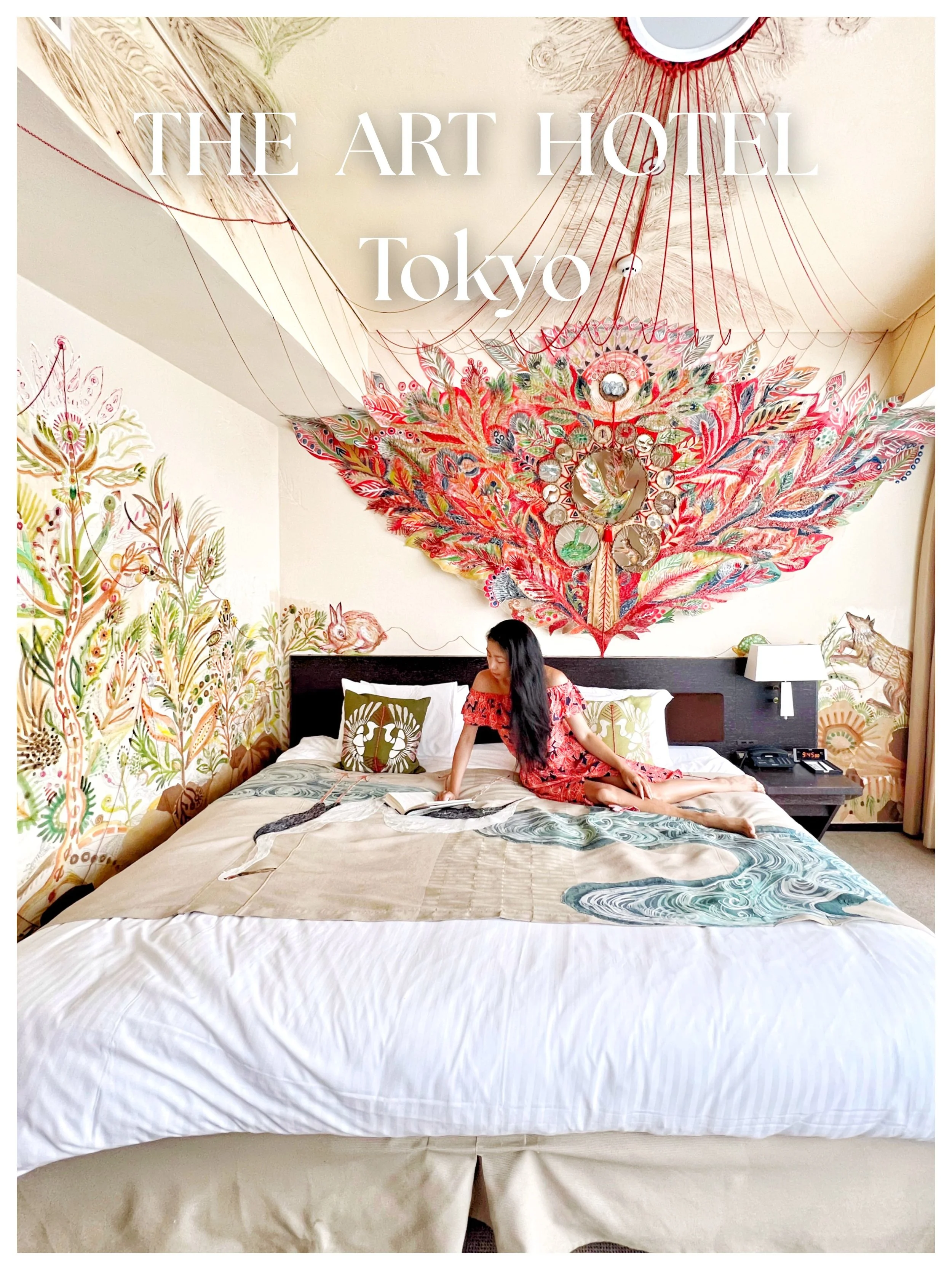 A woman in a red dress with floral patterns is lying on a bed in a hotel room with vibrant, colorful wall art and murals, including a large feather-shaped artwork and animal illustrations, at The Art Hotel Tokyo.