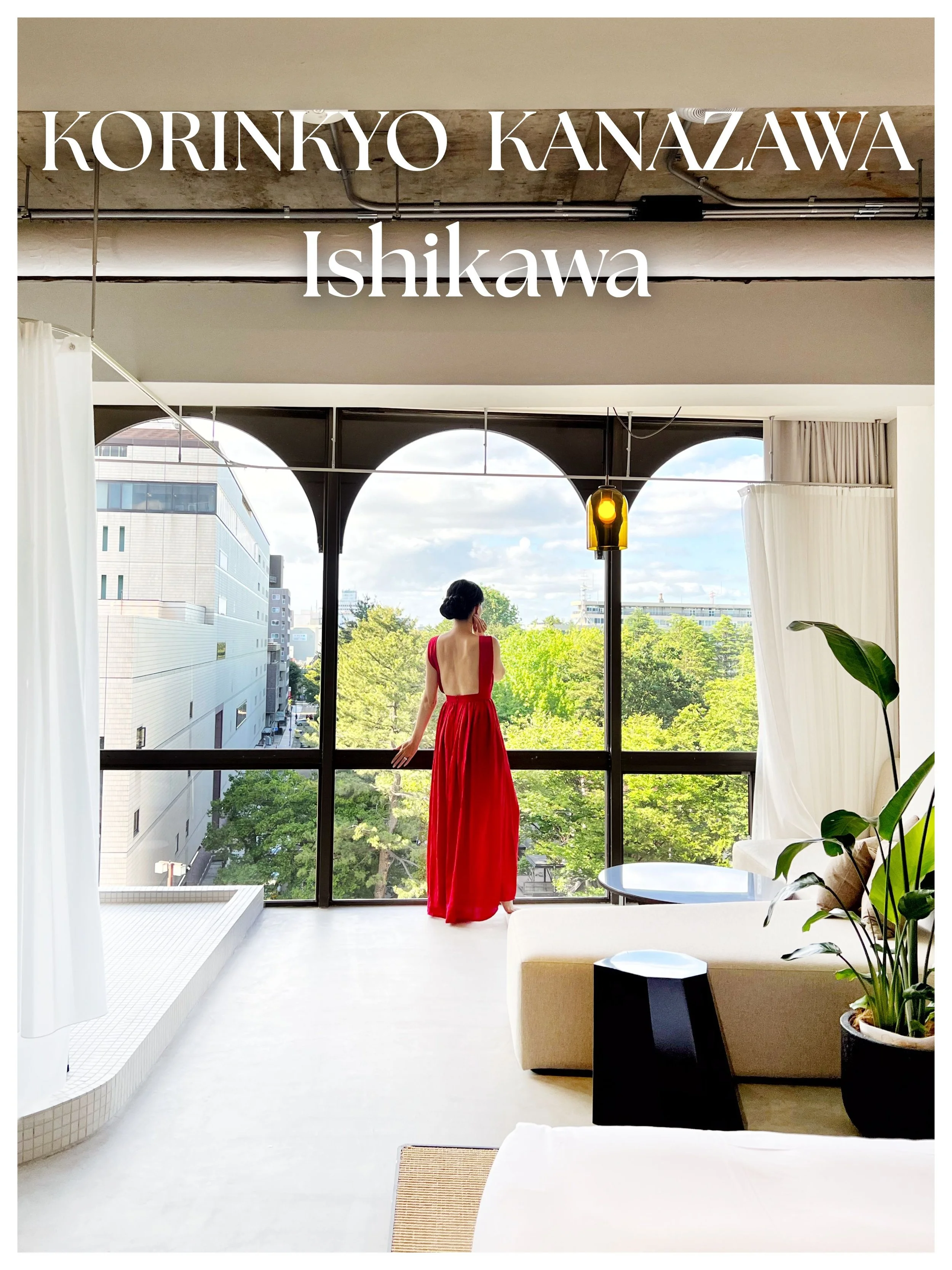 A woman in a red dress standing in a modern interior space, looking out of large windows with a view of trees and buildings outside.