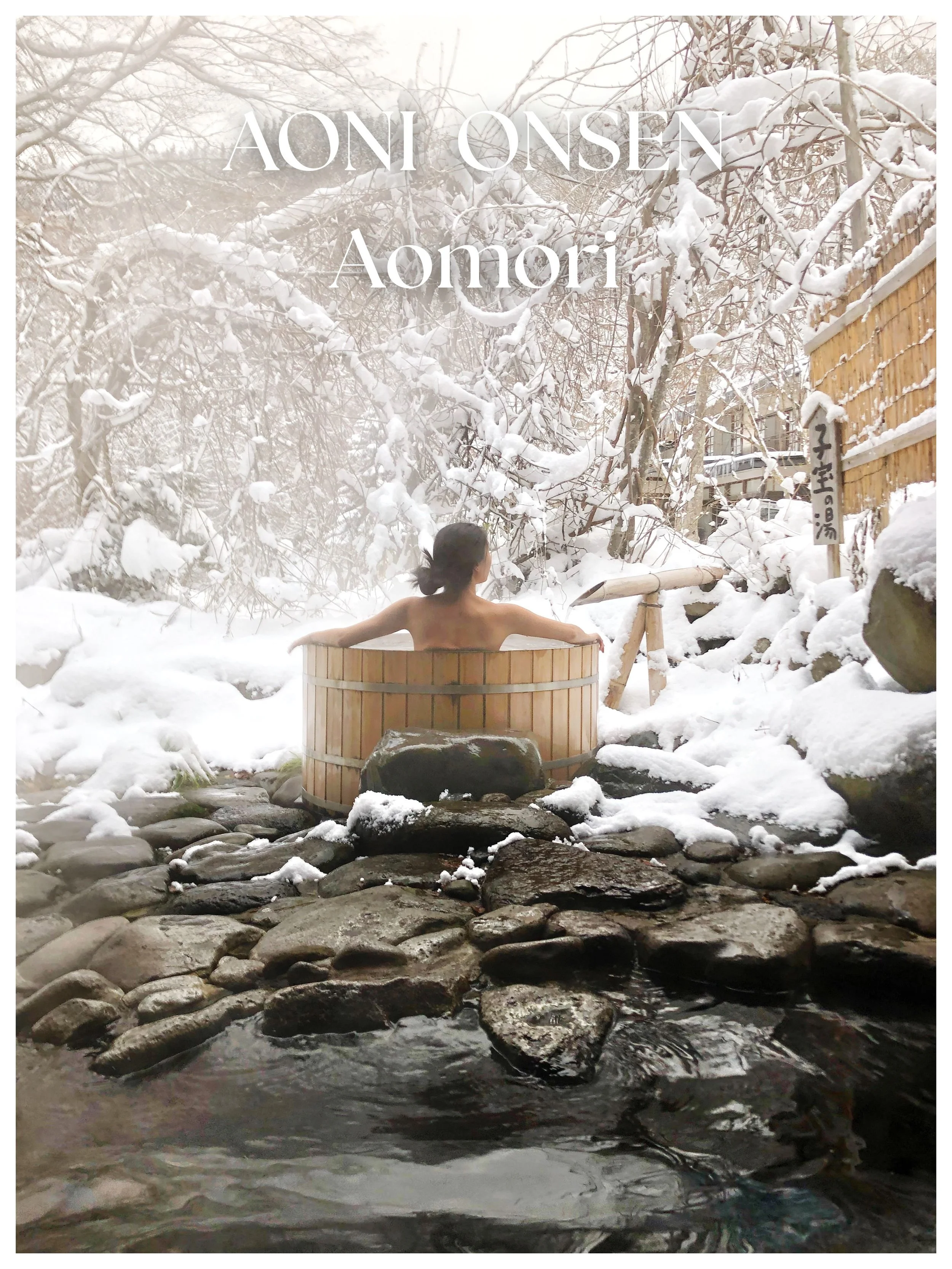 A person soaking in a wooden hot spring bath outdoors surrounded by snow-covered trees and rocks.