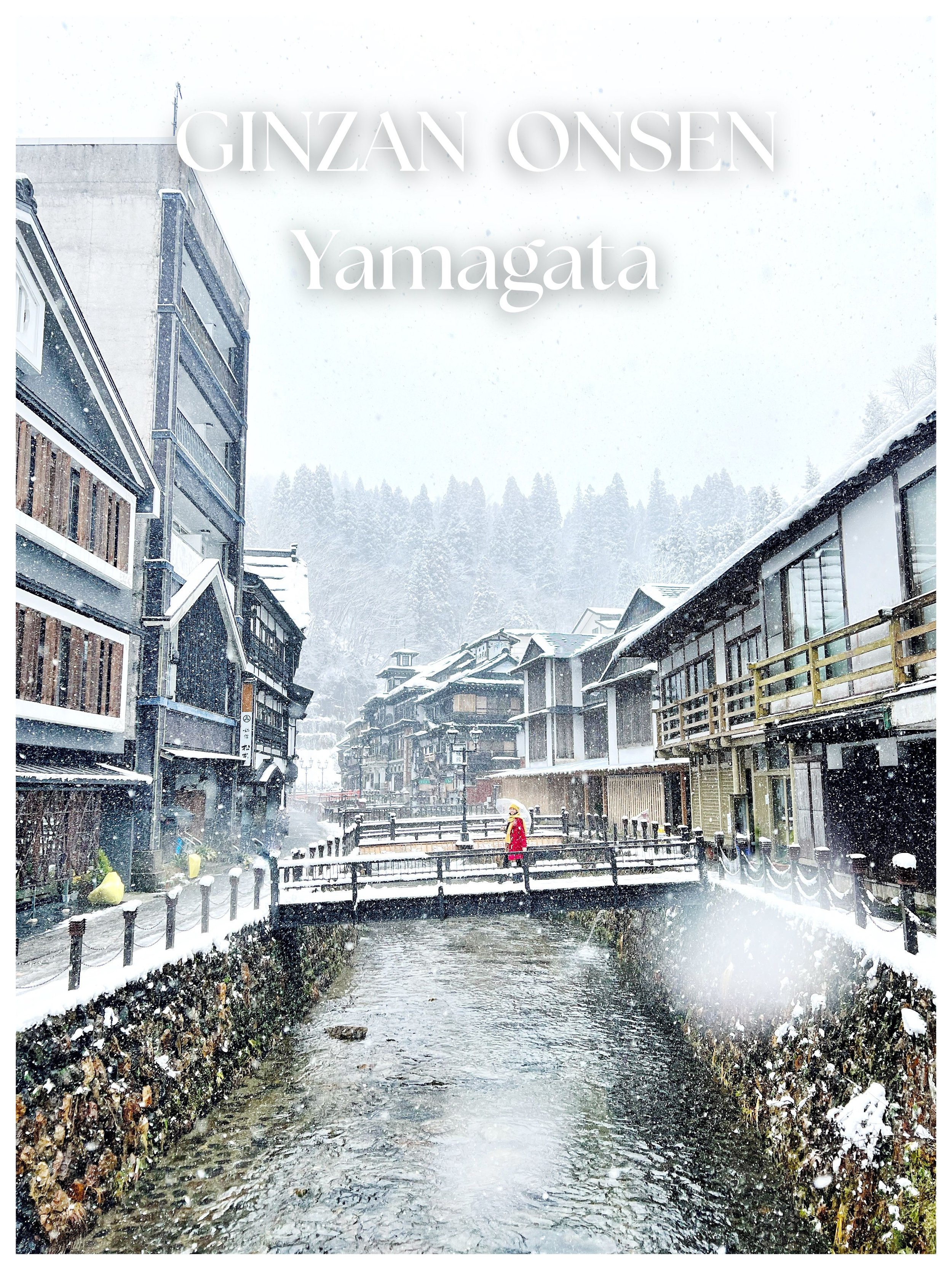 A snow-covered street in Yamagata, Japan, with traditional buildings on both sides and a person in a red coat crossing a small bridge over a canal, during a snowfall.