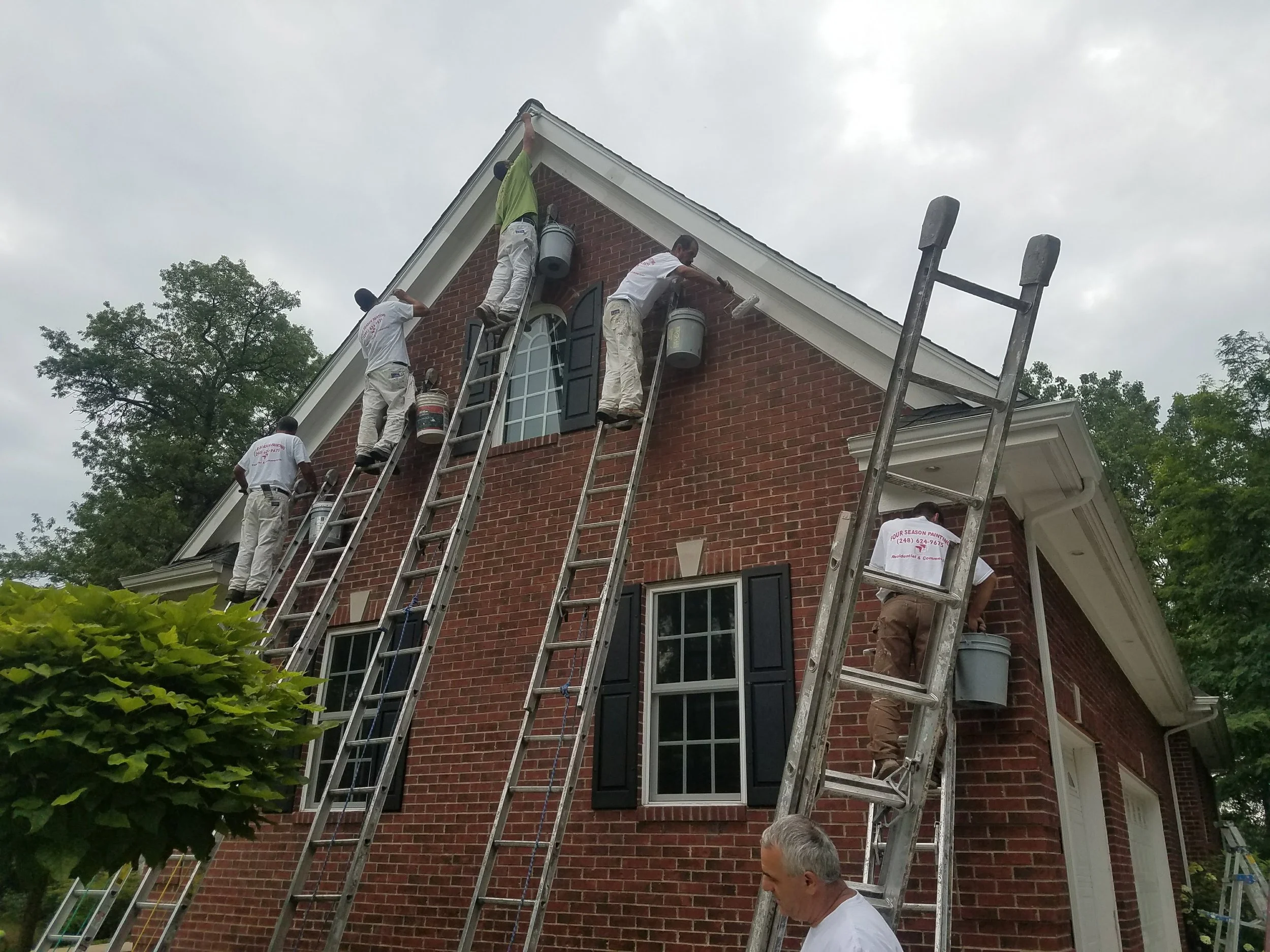 Workers on ladders painting the exterior of a brick house.