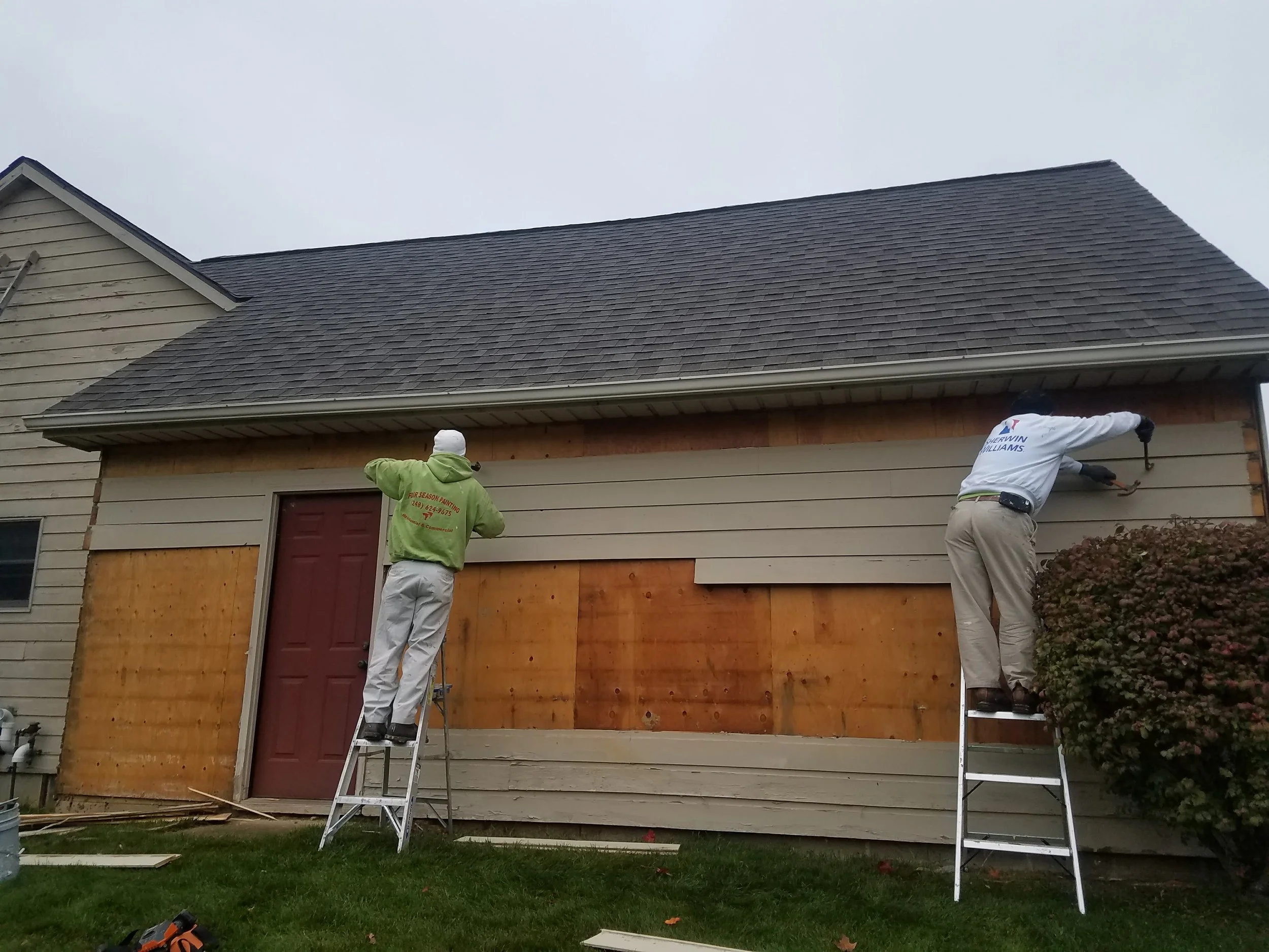 Two workers on ladders installing siding on the exterior of a house.
