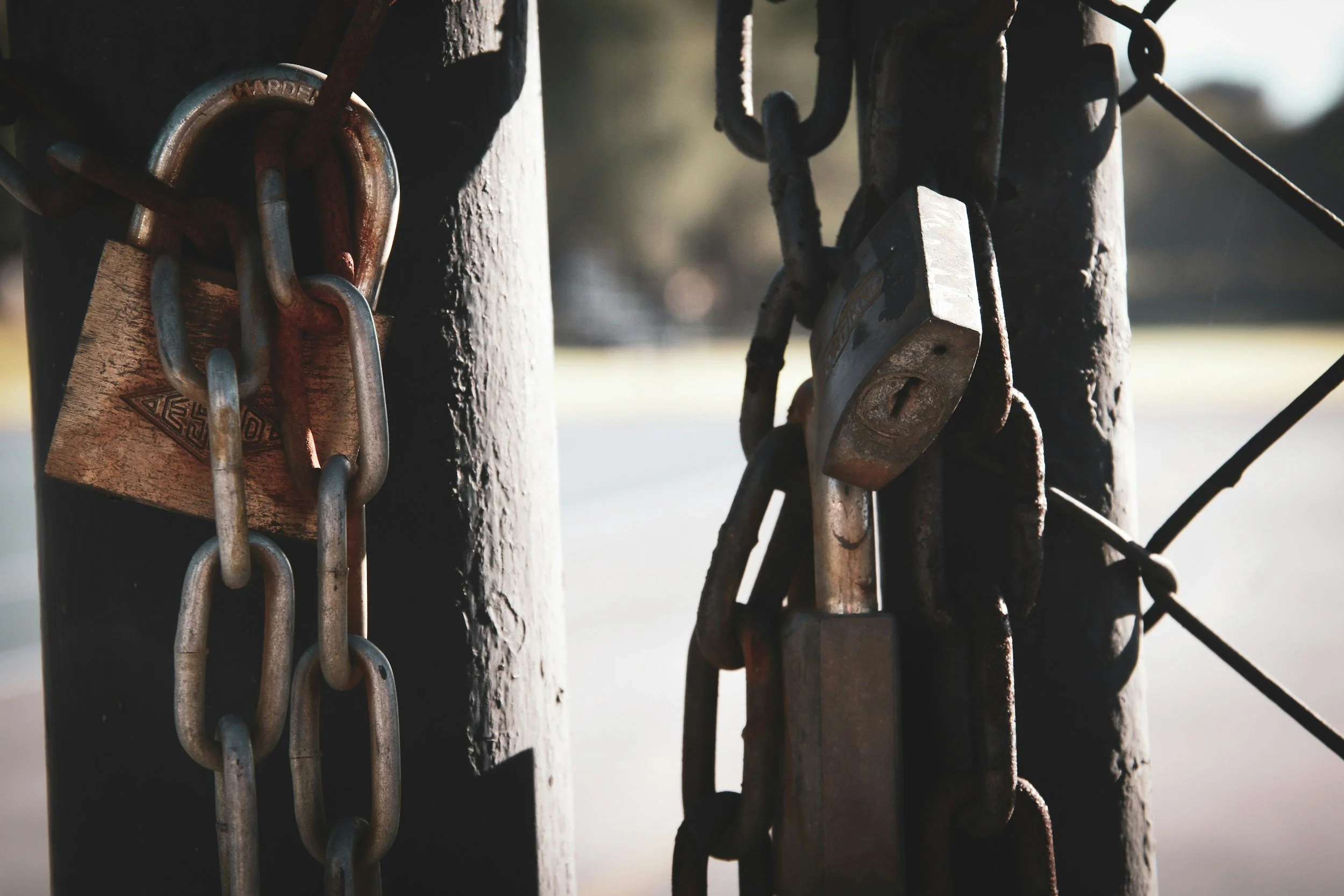 Close-up of a chain and lock securing a gate or fence, with sunlight in the background.