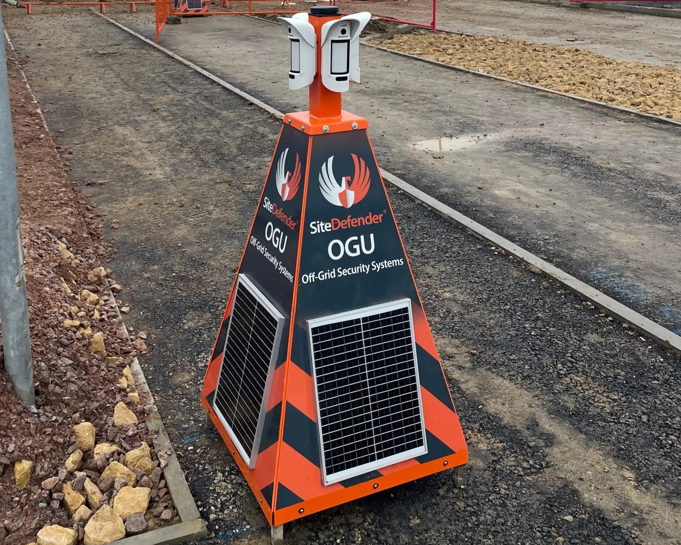 A portable off-grid solar security system with orange and black striped base, solar panels, and sensors on top, placed on a construction site.