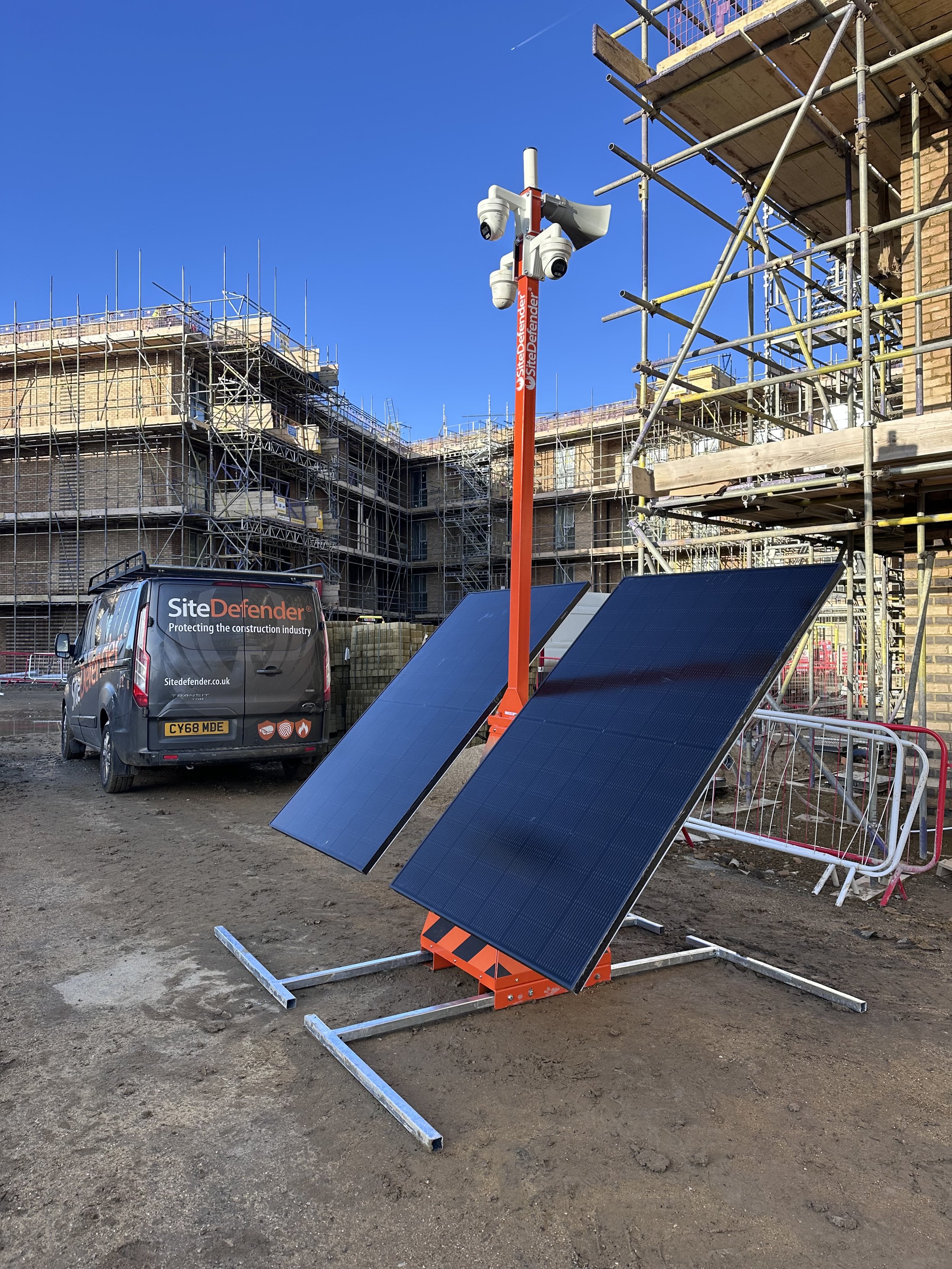 Solar panels installed on a construction site with scaffolding in the background and a Site Defender vehicle parked nearby.