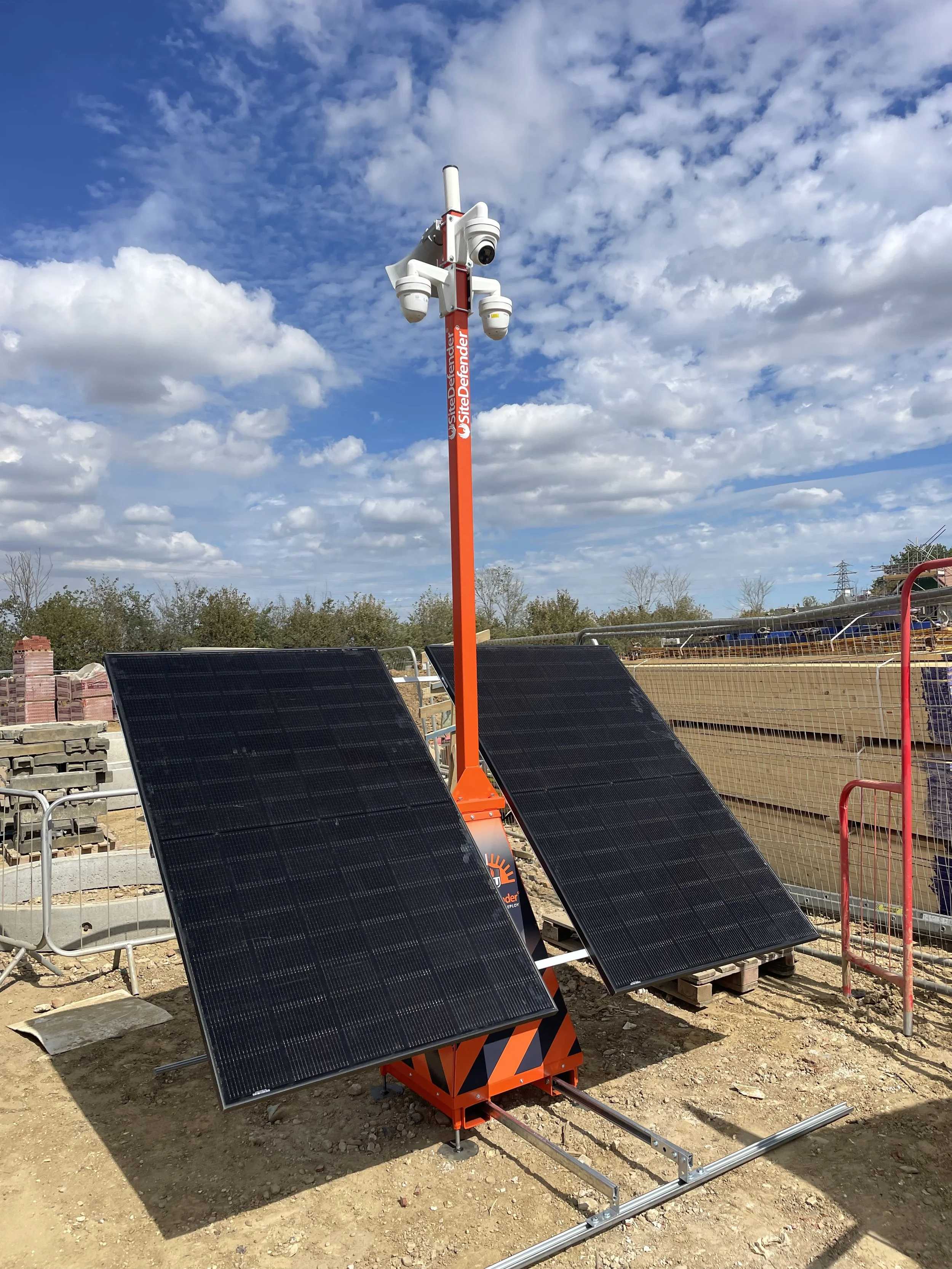 Solar panels and a mobile surveillance camera station on a construction site with blue sky and clouds in the background.