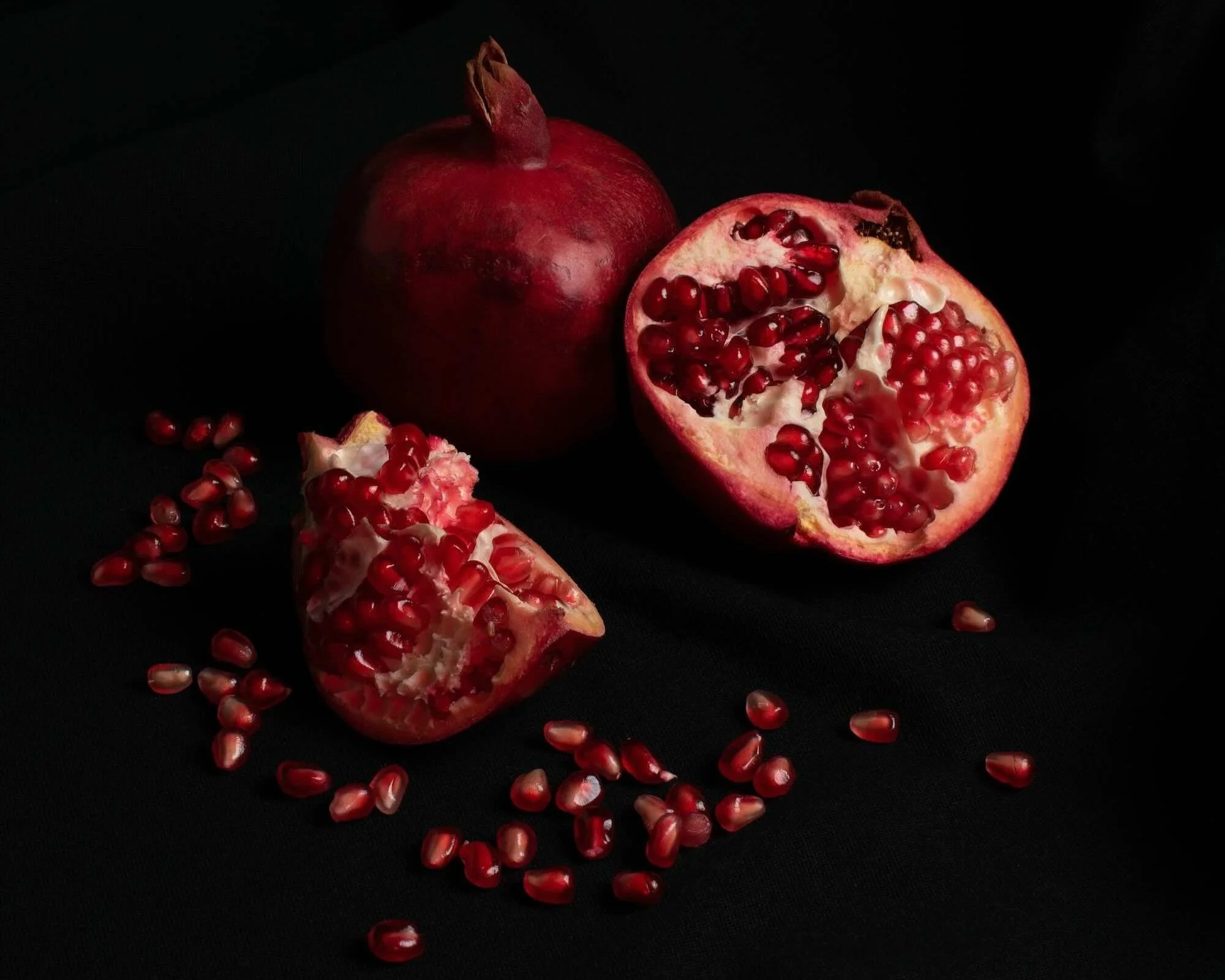 Two Pomegranates, one whole and one cut open with seeds on the table, with a black background